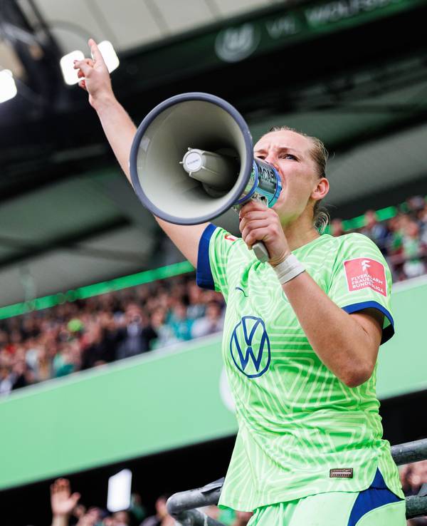 Alexandra Popp vom VfL Wolfsburg steht auf dem Zaun und feiert mit Wolfsburger Fans nach Spielende und spricht durch ein Megaphon der Fans.