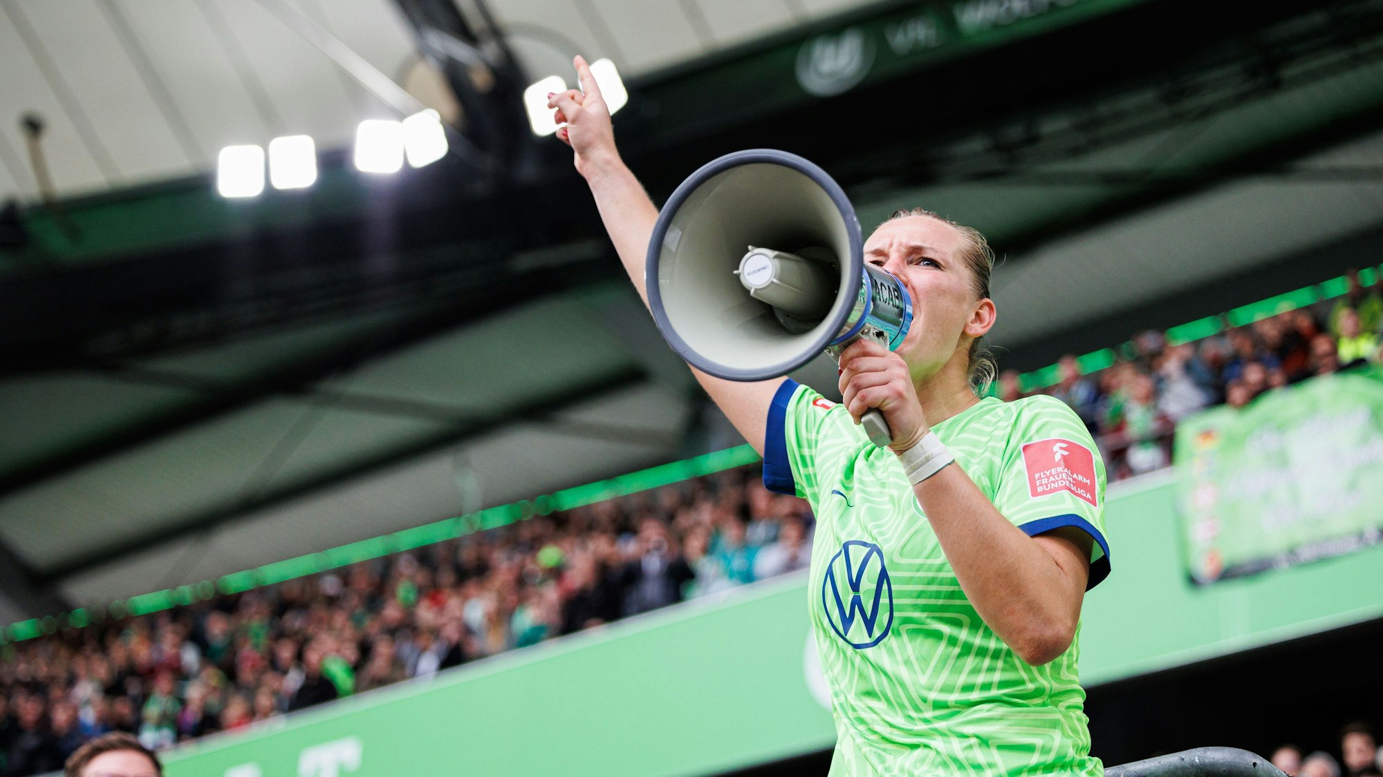 Alexandra Popp vom VfL Wolfsburg steht auf dem Zaun und feiert mit Wolfsburger Fans nach Spielende und spricht durch ein Megaphon der Fans.