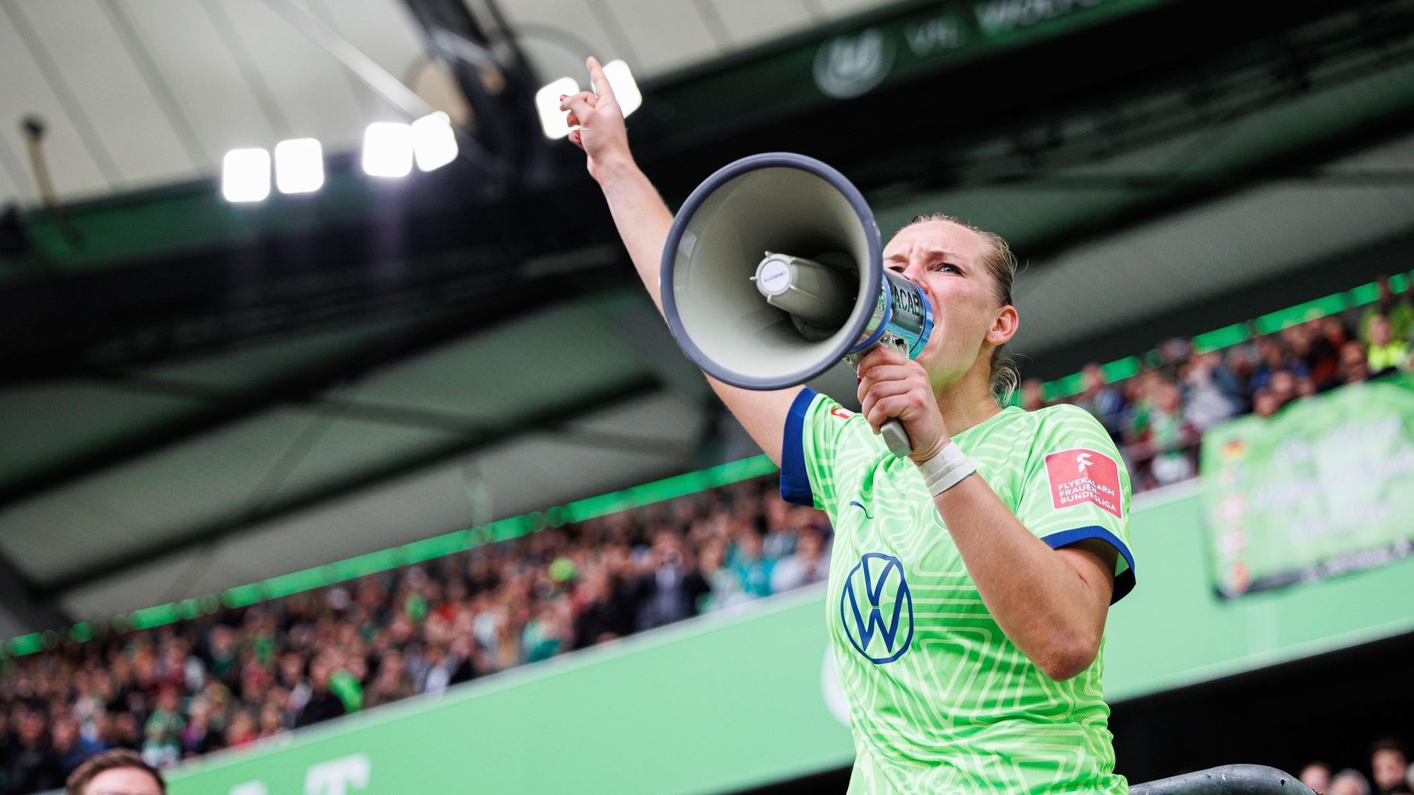 Alexandra Popp vom VfL Wolfsburg steht auf dem Zaun und feiert mit Wolfsburger Fans nach Spielende und spricht durch ein Megaphon der Fans.