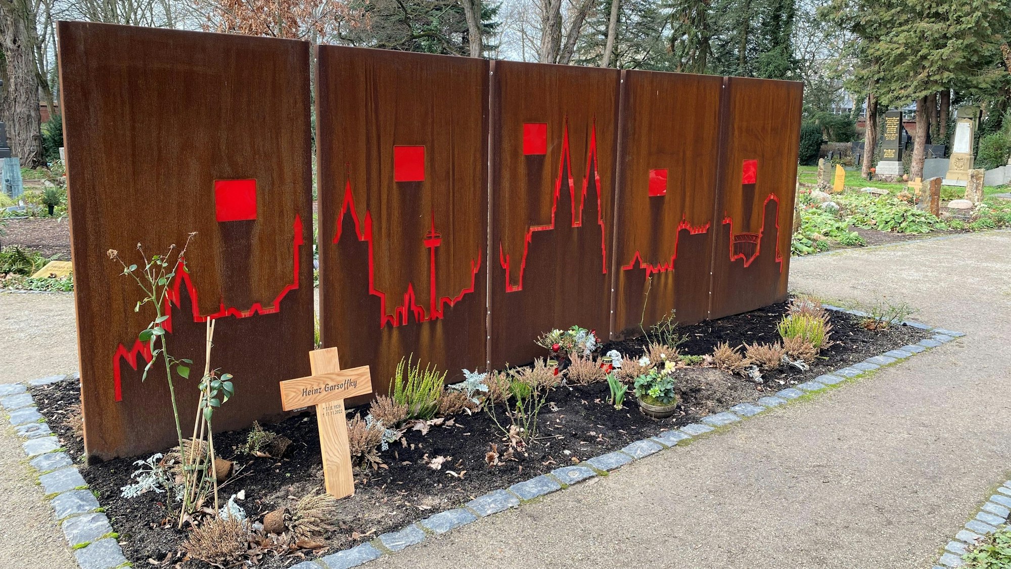 Rolf Bungerts Grabstätte auf Melaten. Das Urnengrab befindet sich unter der Domsilhouette. In die roten Quadrate kommen noch die Namen der Verstorbenen.