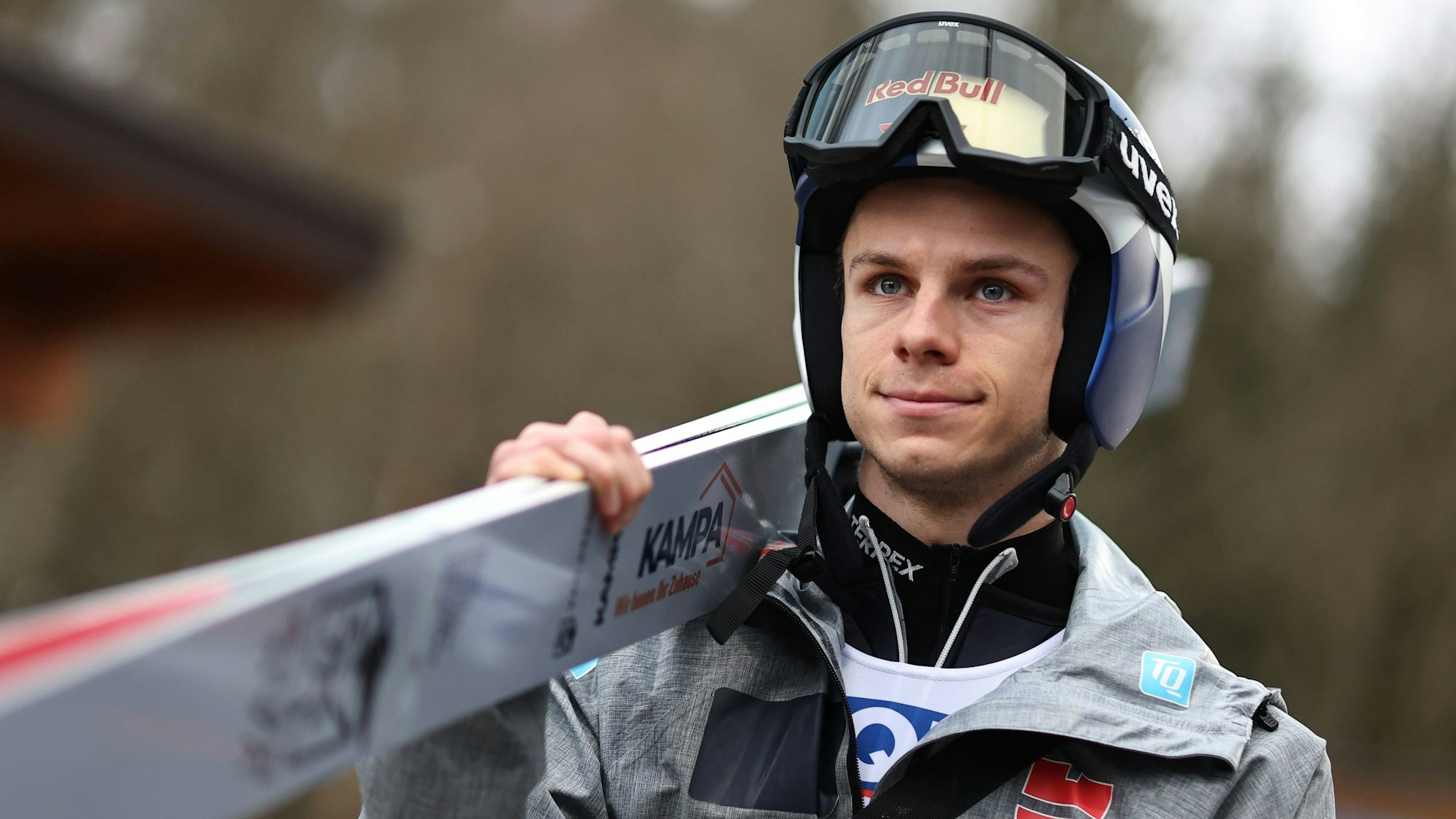 Andreas Wellinger (Deutschland) kommt zum Training in Bischofshofen. Er trägt einen Helm mit hochgezogener Skibrille und eine Trainingsjacke. Seine Skier trägt er auf der rechten Schulter.