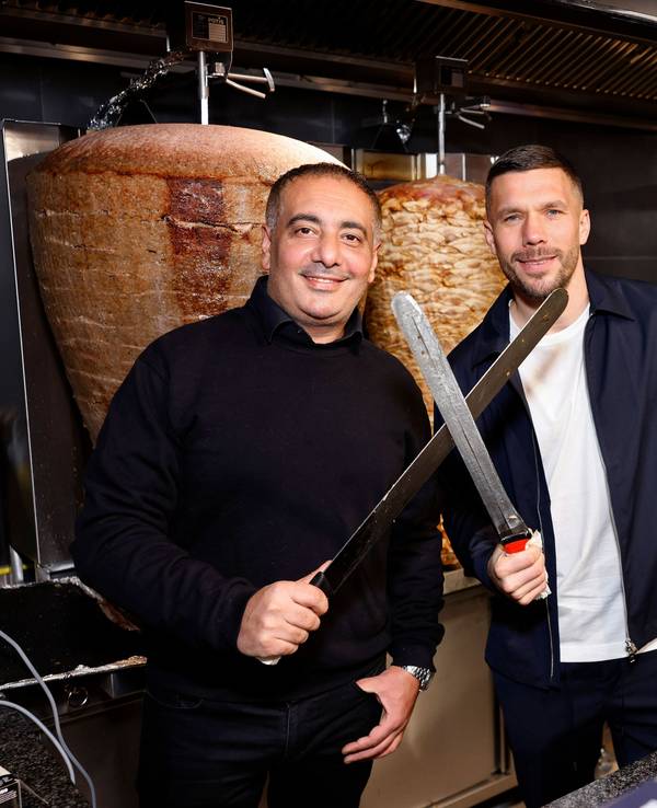 Geschäftsführer Metin Dag und Fußballer Lukas Podolski stehen hinter der Theke bei Mangal-Döner.