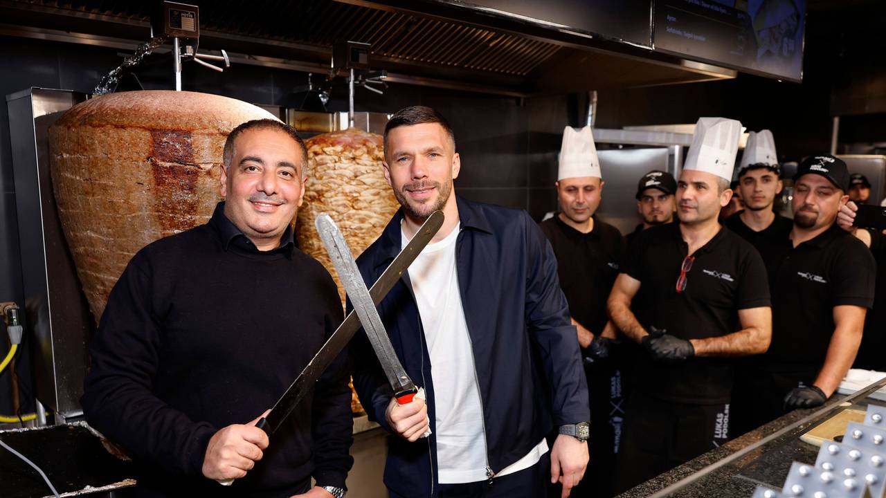 Geschäftsführer Metin Dag und Fußballer Lukas Podolski stehen hinter der Theke bei Mangal-Döner.