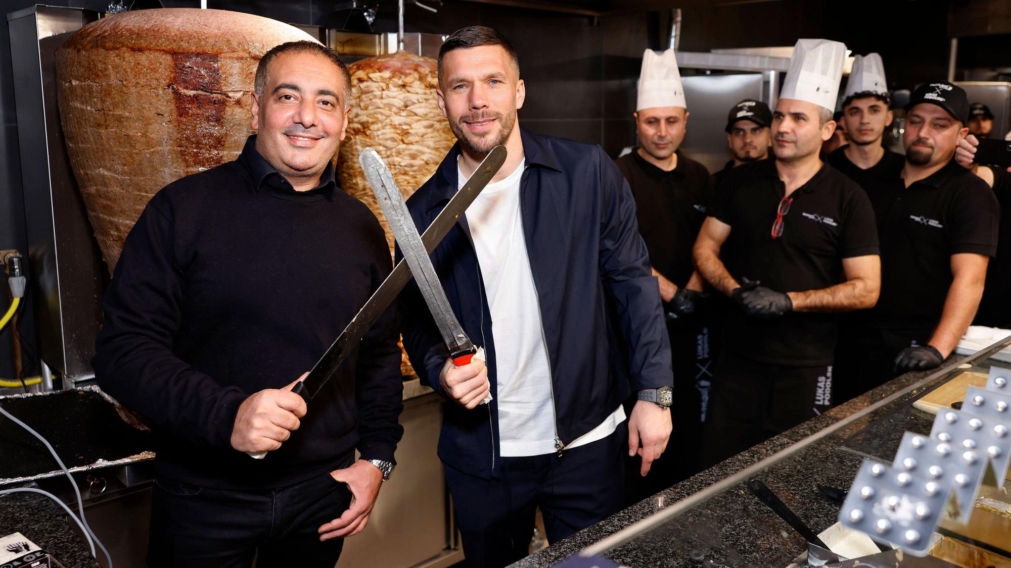 Geschäftsführer Metin Dag und Fußballer Lukas Podolski stehen hinter der Theke bei Mangal-Döner.