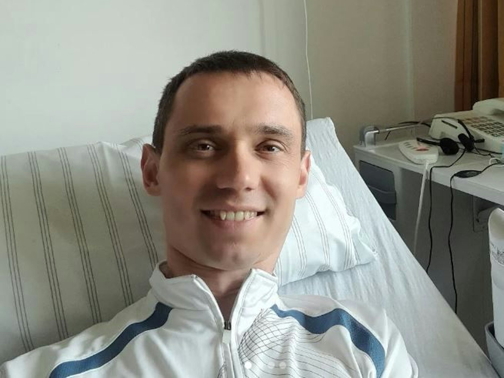 Ein Mann liegt in einem Krankenbett und schaut in die Kamera.