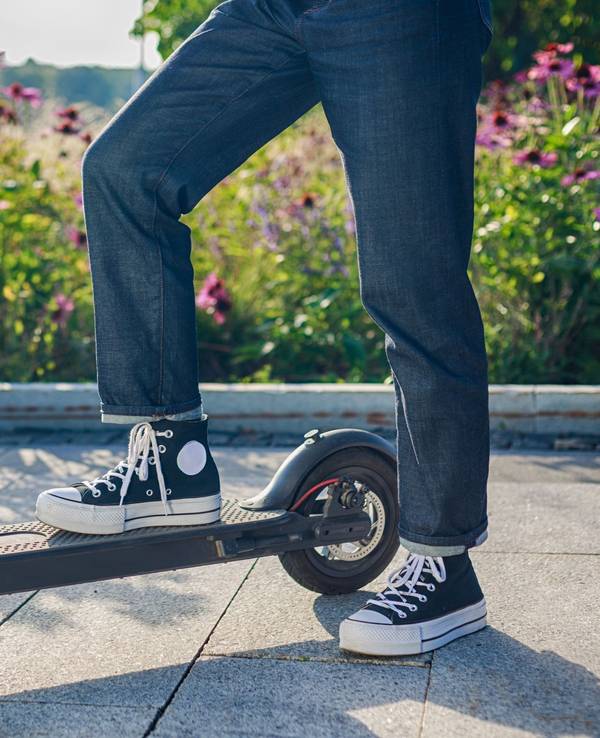 Frau steht mit einem Bein auf ihrem E - Scooter
