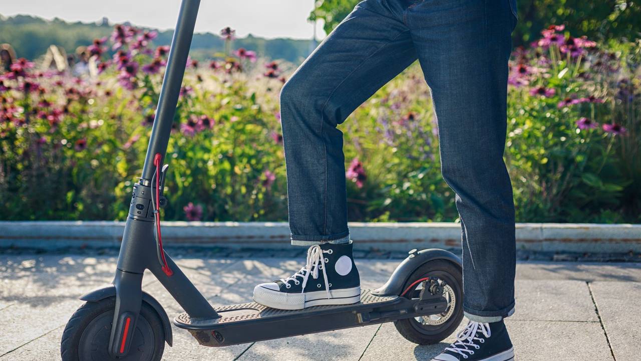 Frau steht mit einem Bein auf ihrem E - Scooter