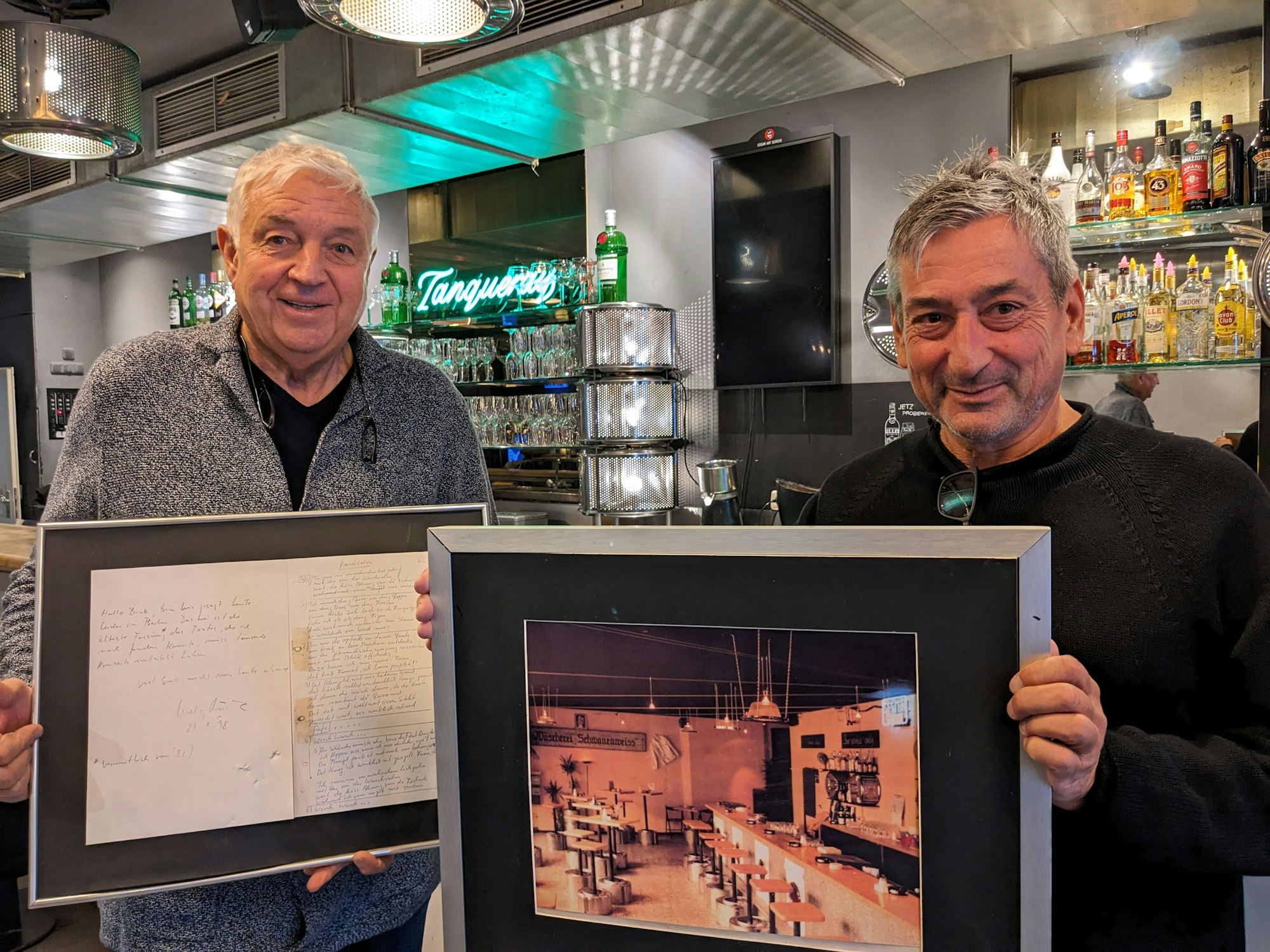 Die Waschsalon-Inhaber Dirk Holzmann (l.) und Jürgen Walter präsentieren ihre Schätze: Holzmann hält den eingerahmten Notizzettel zum Song „Waschsalon“ von Wolfgang Niedecken und Walter hält ein Foto vom Café Waschsalon in der Friesenstraße.