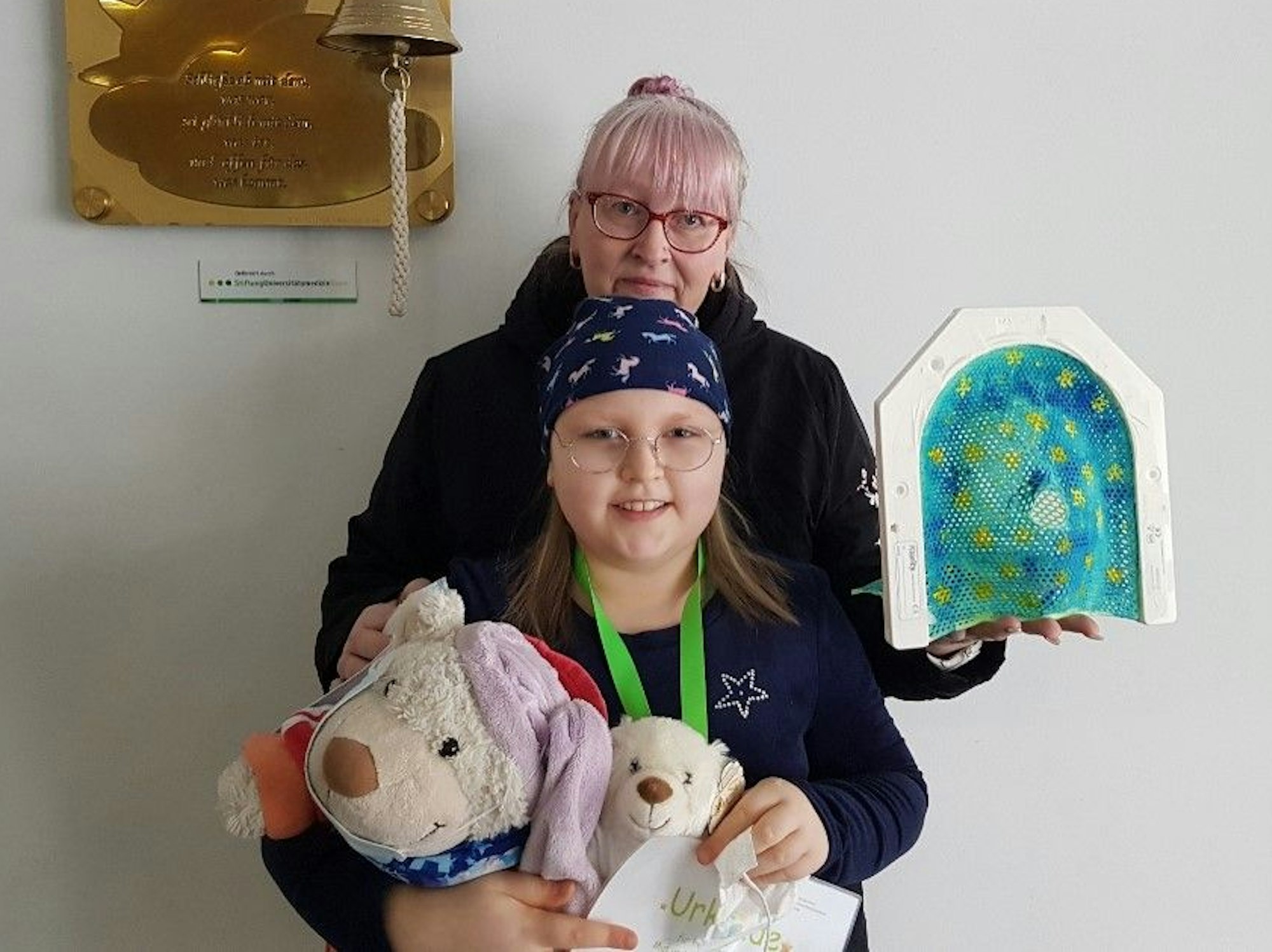 Eine Frau steht hinter ihrer Tochter und schaut in die Kamera.