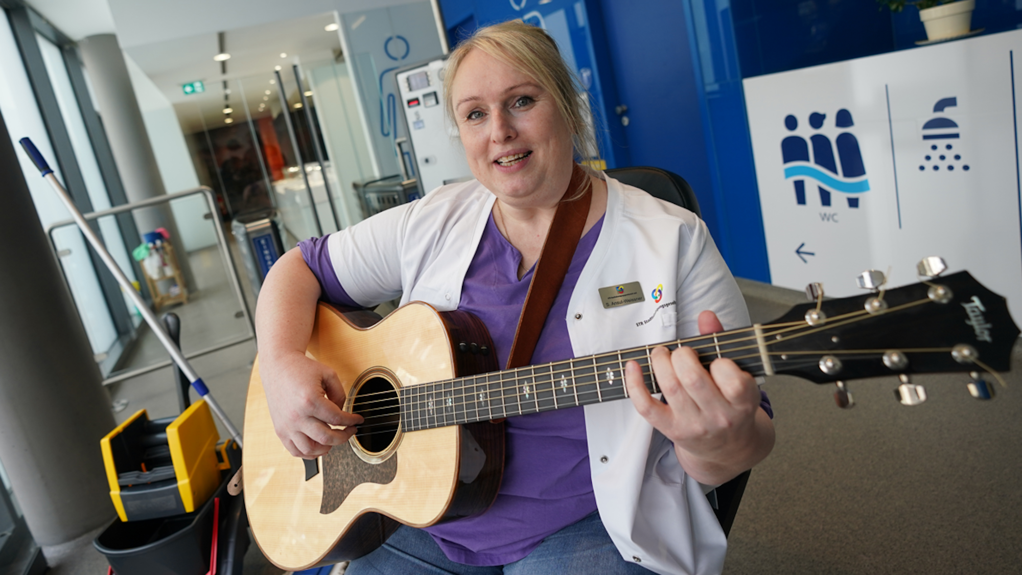 Stefanie Ansul-Weissner, Reinigungskraft der STR Stadtteilreinigungsgesellschaft mbH, spielt in den Räumlichkeiten der öffentlichen Toilette Am Niederhafen auf ihrer Gitarre und singt dazu ein Lied.