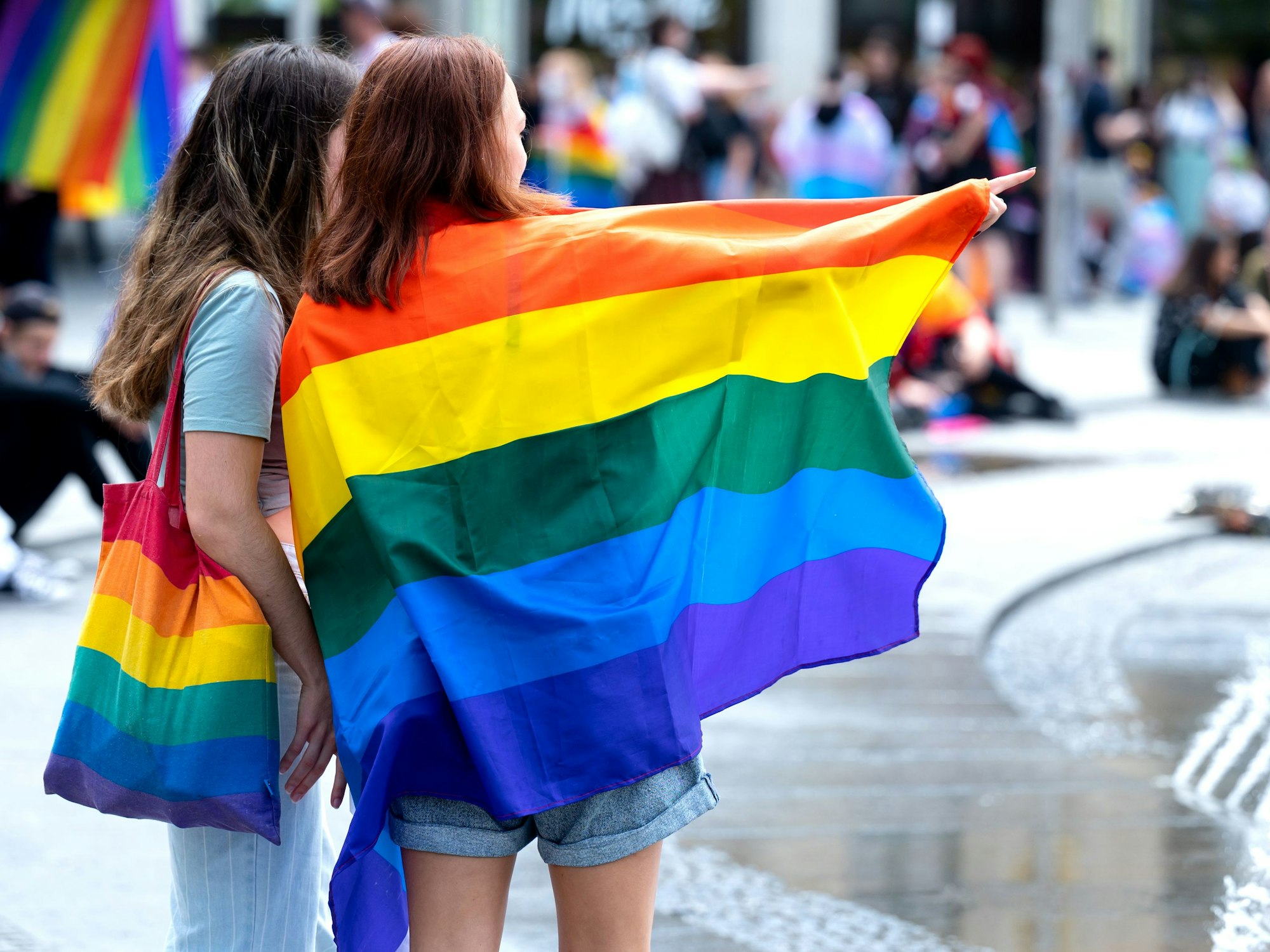 Teilnehmer des Christopher Street Days (CSD) stehen bei sommerlichen Temperaturen mit Regenbogenfahne an einem Springbrunnen.