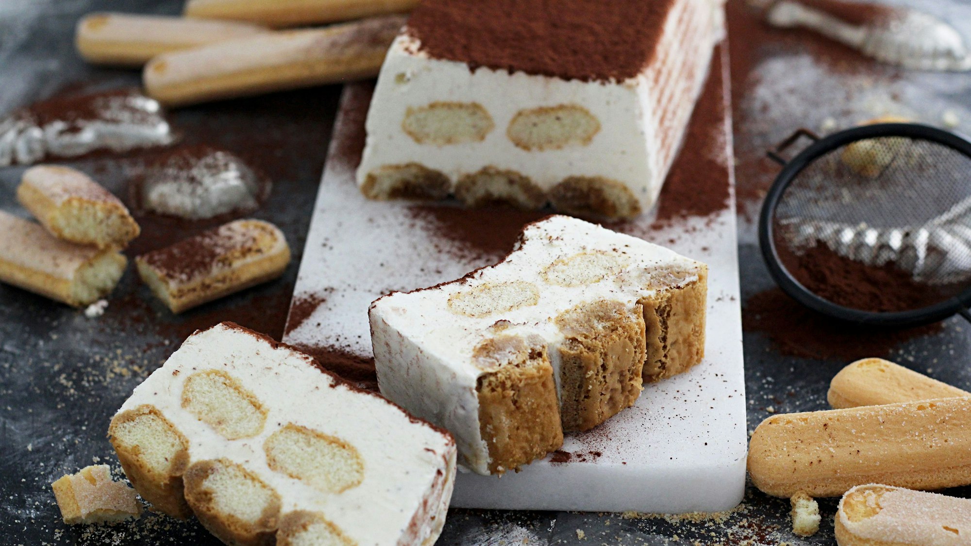Ein Tiramisu liegt in Scheiben geschnitten auf einem Dessertteller.