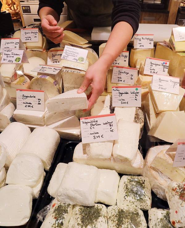 Eine Mitarbeiterin sortiert an der Käsetheke verschiedene Sorten Käse.