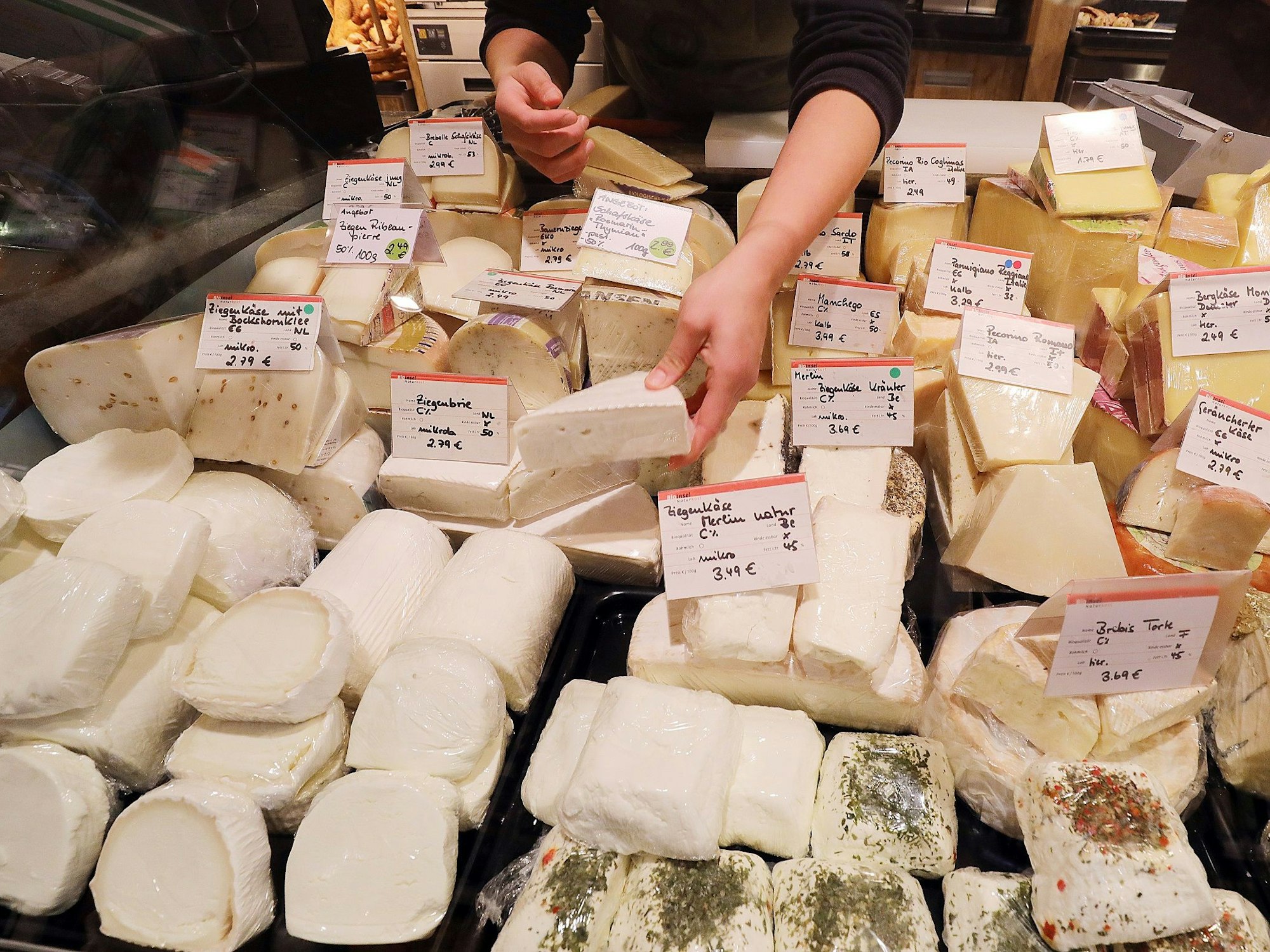 Eine Mitarbeiterin sortiert an der Käsetheke verschiedene Sorten Käse.