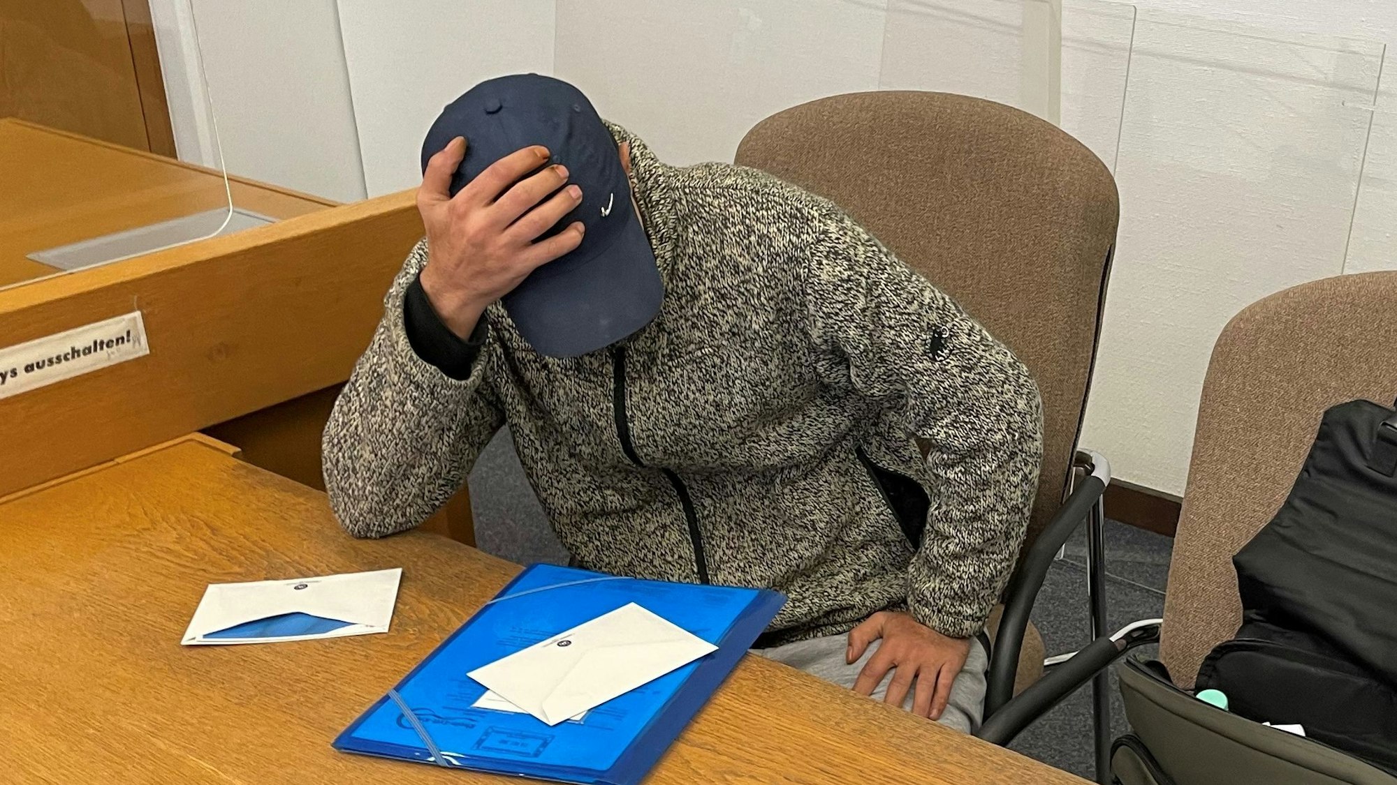 Angeklagter versteckt sich vor Gericht hinter seiner Kappe und seiner Hand.