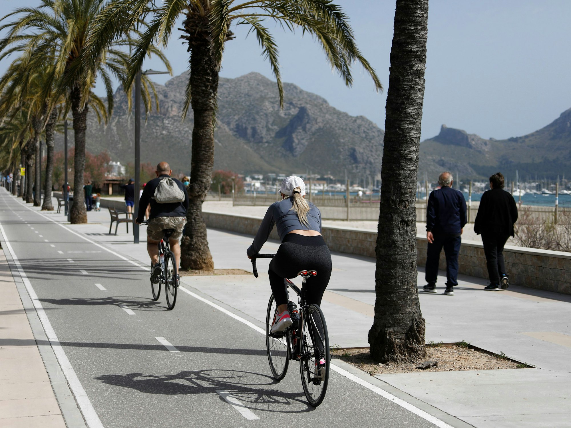 Menschen fahren im April 2021 am Hafen von Pollença auf der Insel Mallorca mit dem Fahrrad. Schon bald soll ein neuer Radweg das Zentrum von Mallorca mit dem Flughafen verbinden.