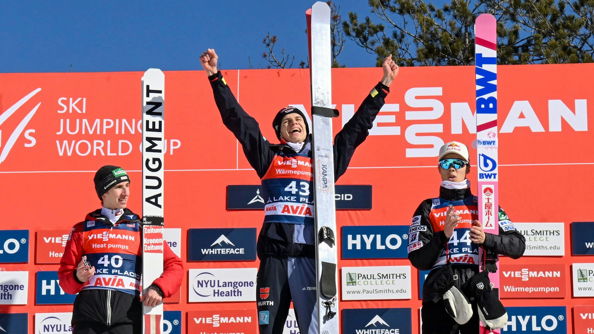 Daniel Tschofenig, Andreas Wellinger und Ryoyu Kobayashi auf dem Siegerpodest in Lake Placid. Wellinger reißt jubelnd die Arme hoch.
