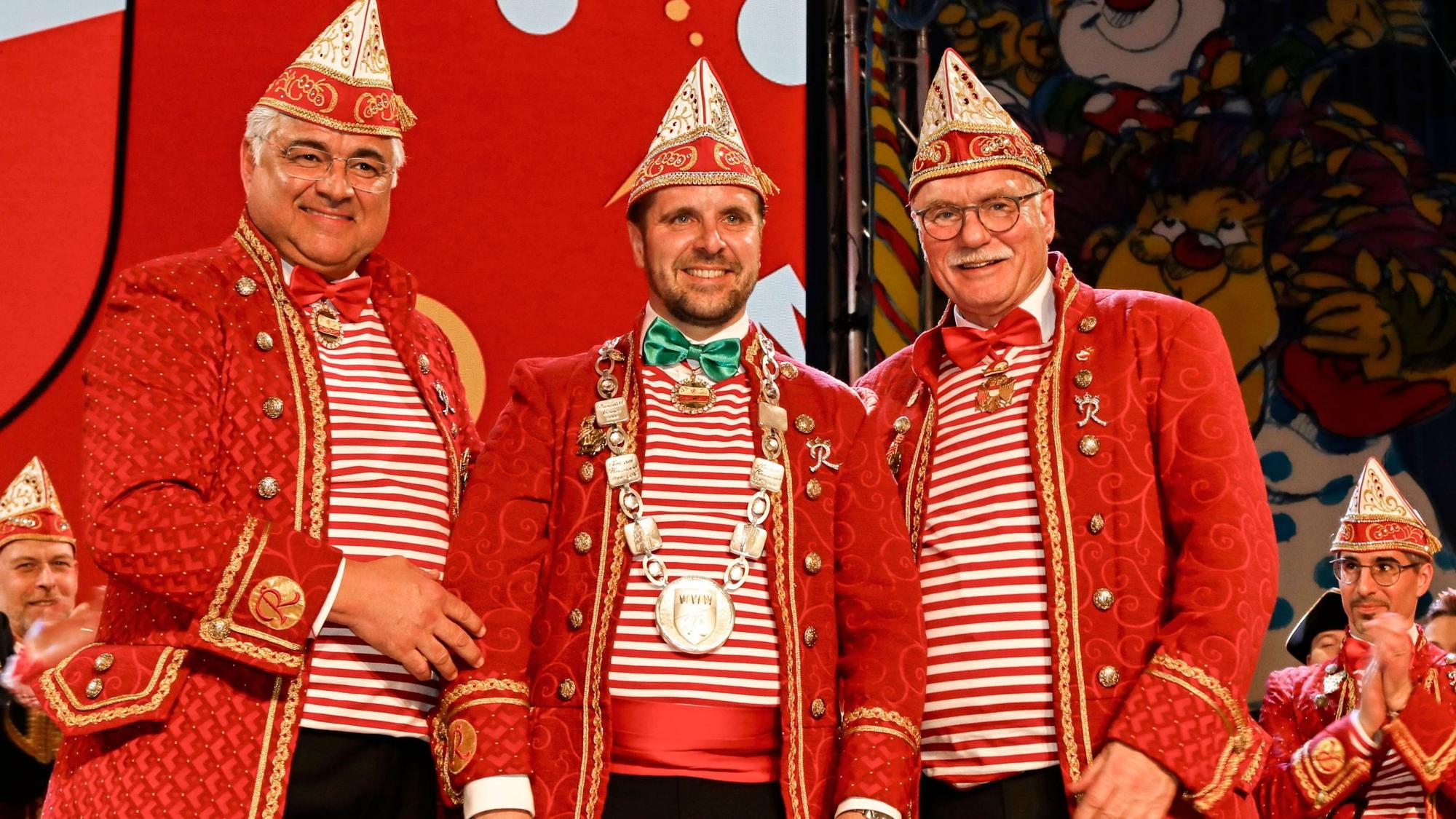 Drei Männer in roten Anzügen stehen gemeinsam für ein Foto auf der Bühne.