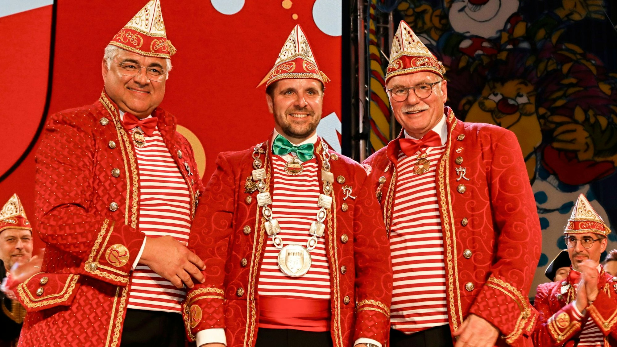 Drei Männer in roten Anzügen stehen gemeinsam für ein Foto auf der Bühne.