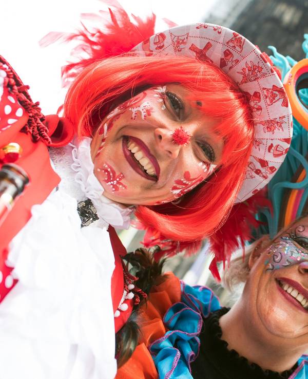 Das Symbolfoto zeigt zwei zu Weiberfastnacht verkleidete Frauen mit bunten Hüten und Karnevalsschminke im Gesicht. Im Hintergrund steht der Kölner Dom.