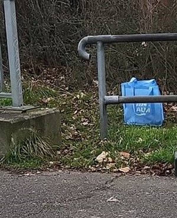 Eine Einkaufstasche mit dem Namen eines Discounters steht am Wegesrand.