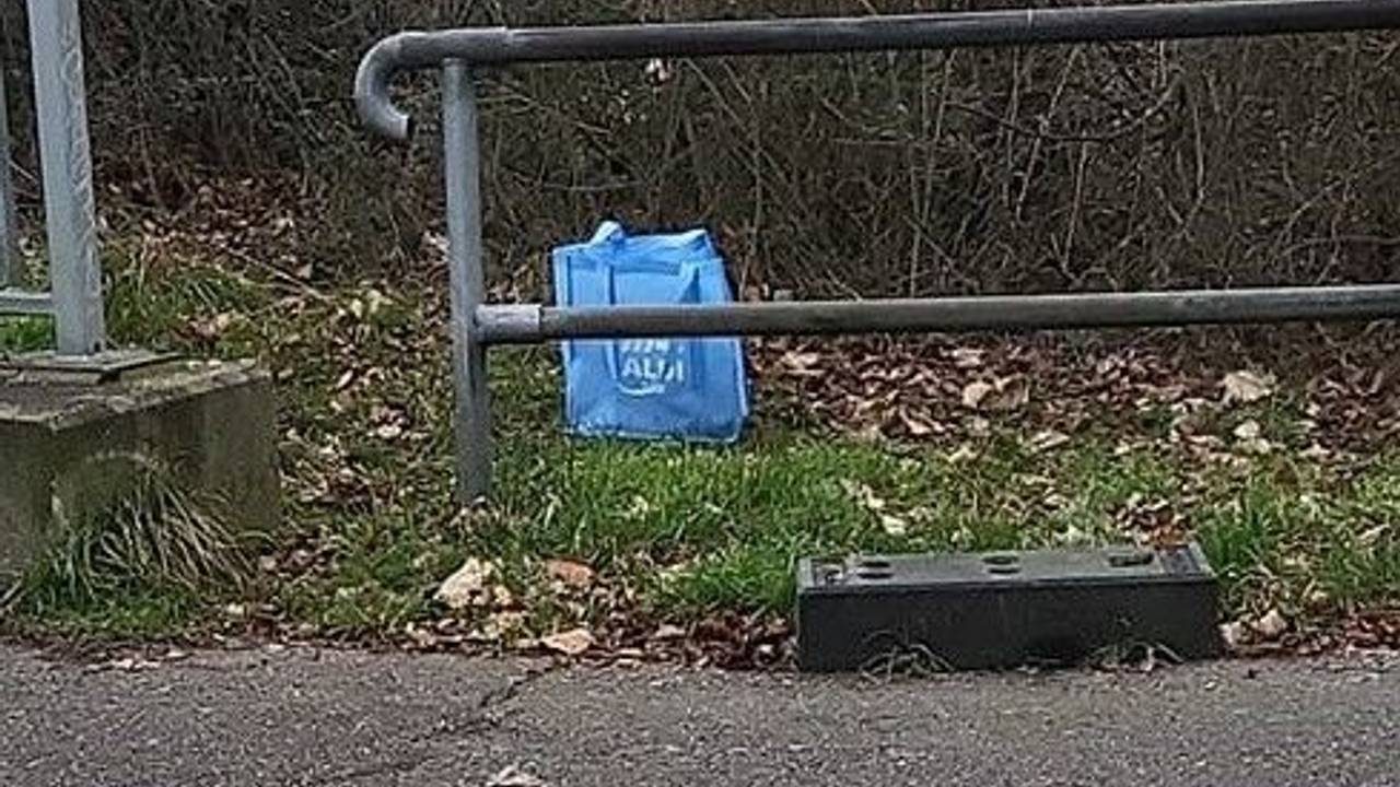Eine Einkaufstasche mit dem Namen eines Discounters steht am Wegesrand.