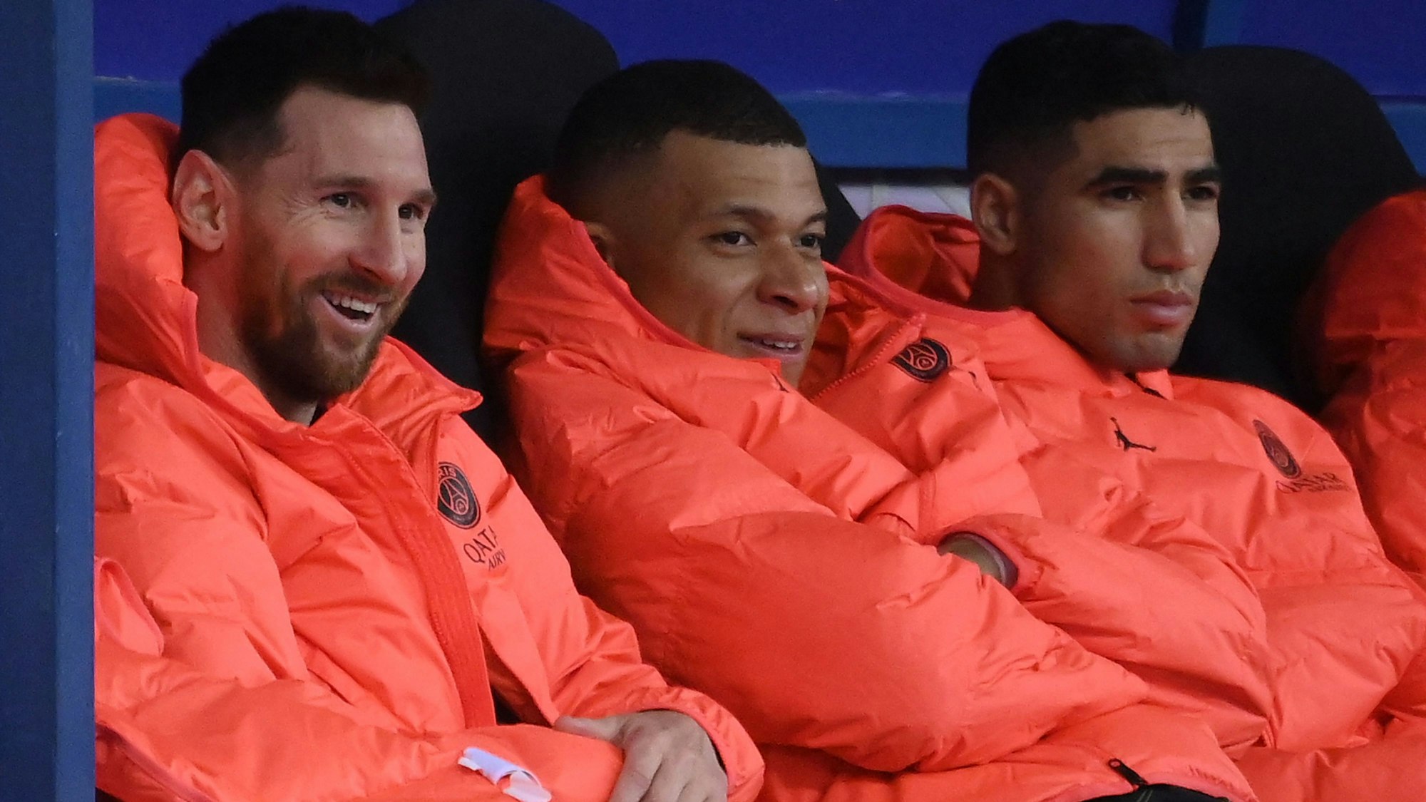 Lionel Messi, Kylian Mbappé und Achraf Hakimi sitzen nebeneinander auf der Auswechselbank.