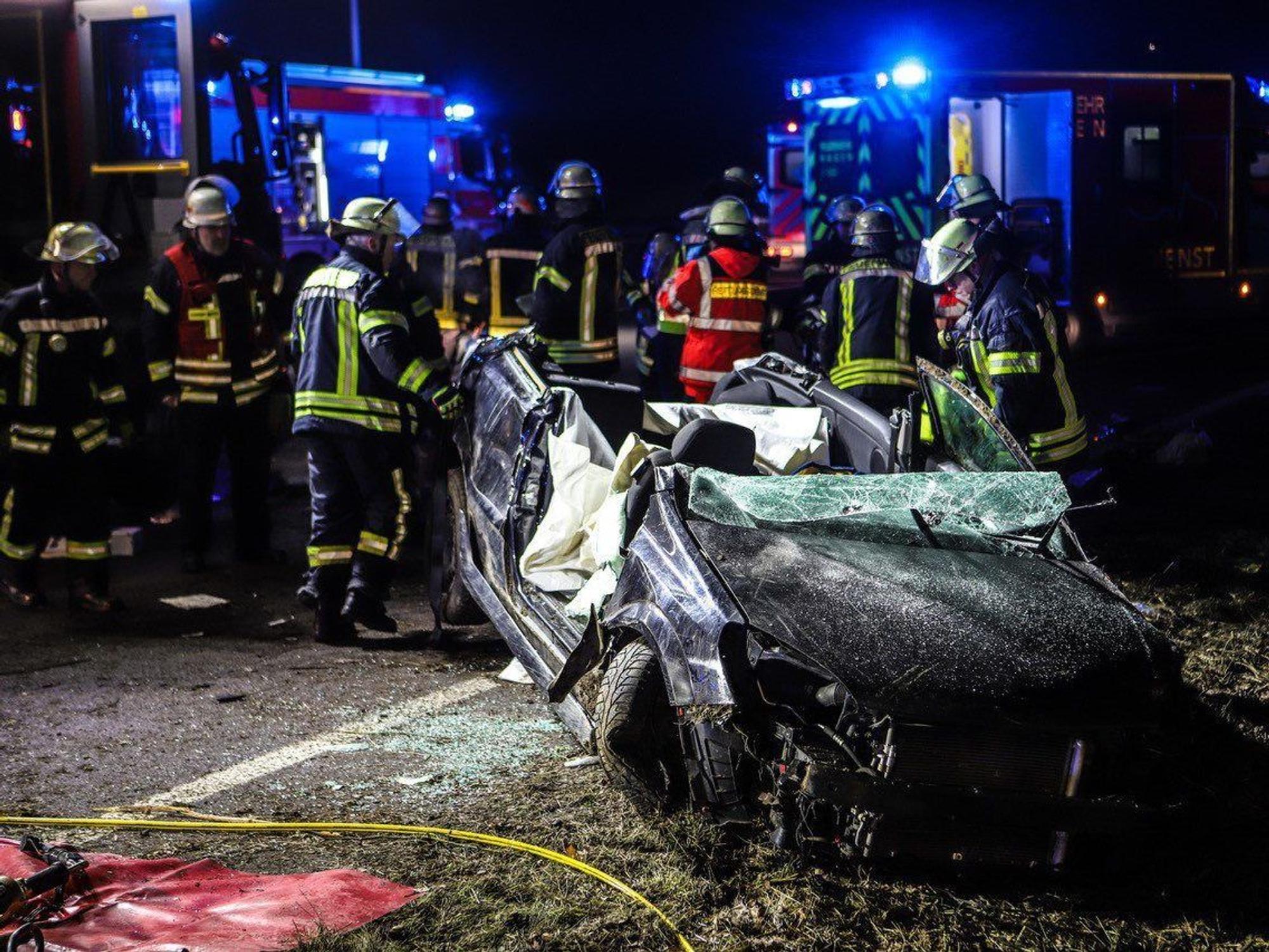 Einsatzkräfte stehen auf der A1 an einer Unfallstelle neben einem komplett zerstörten Auto.