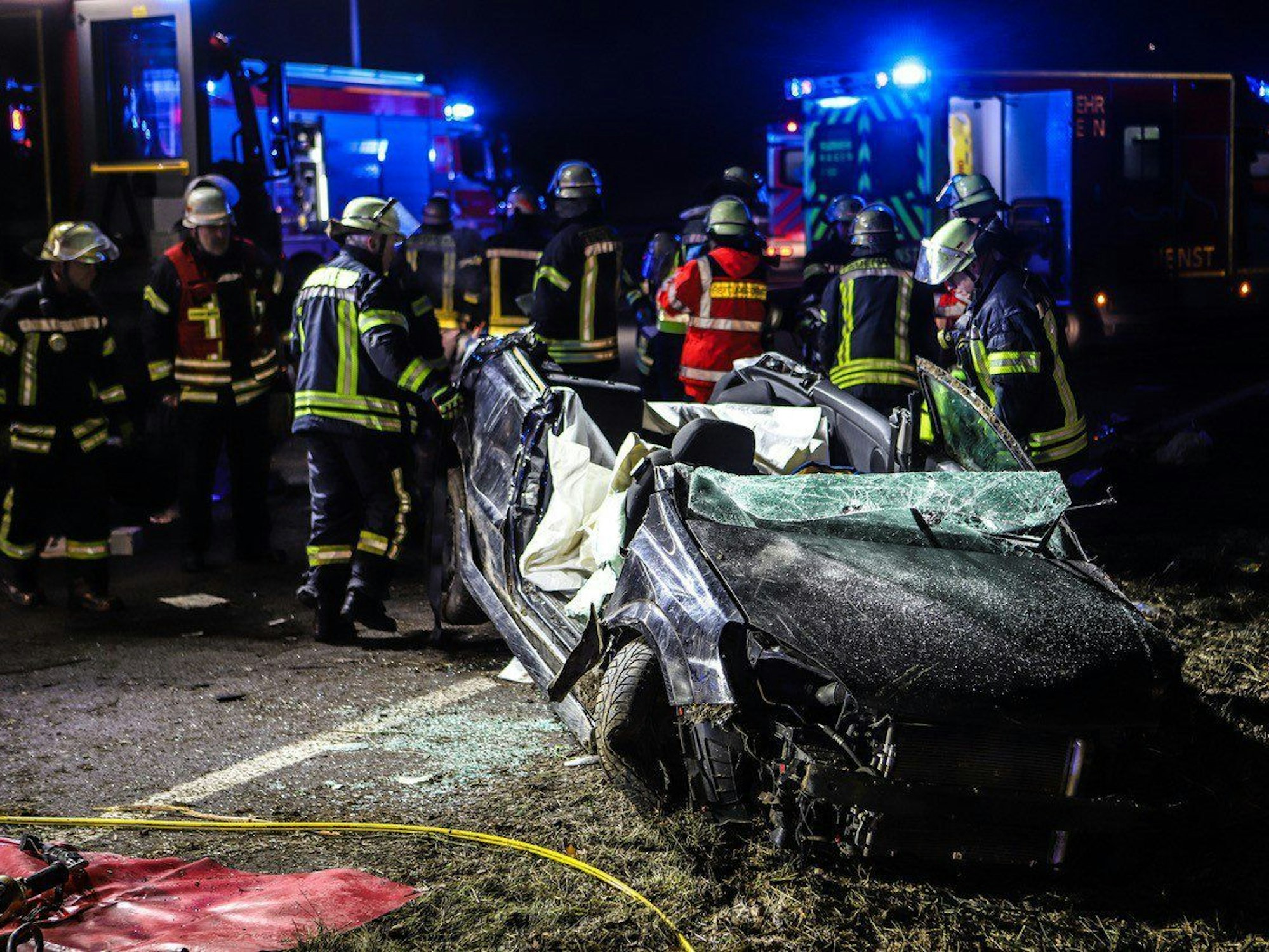 Einsatzkräfte stehen auf der A1 an einer Unfallstelle neben einem komplett zerstörten Auto.