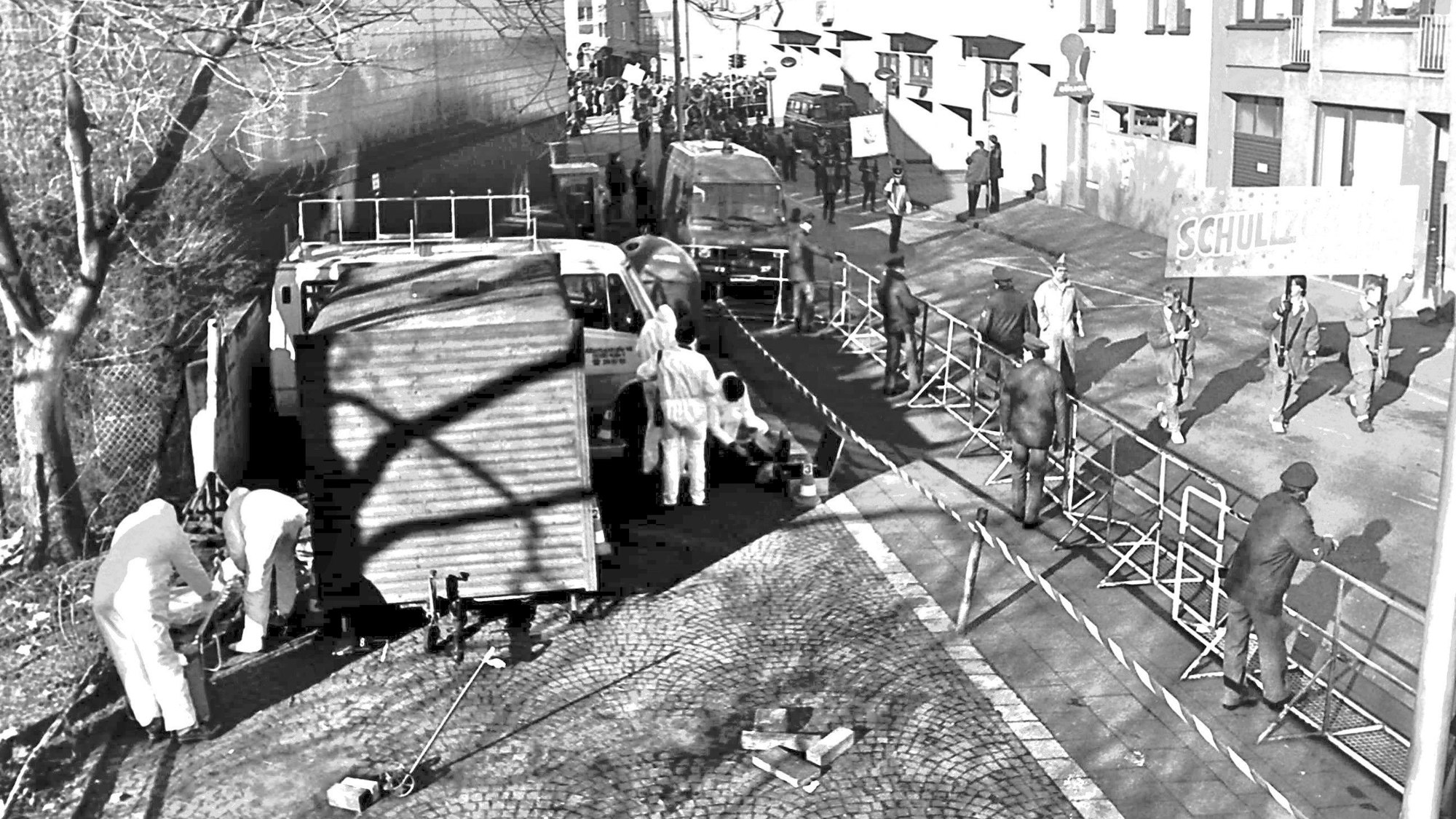 Polizeikräfte wuseln um den Imbisswagen herum, hinter dem die Leiche von Petra Nohl gefunden wurde. Auf der angrenzenden Straße zieht ein Karnevalsumzug vorbei.