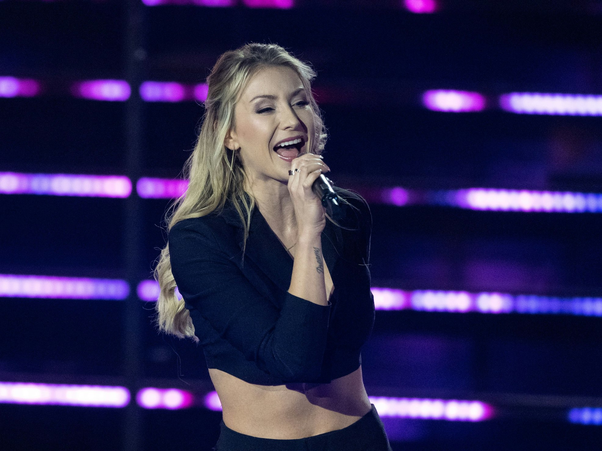 Die deutsche Sängerin Anna-Carina Woitschack steht in der Fernsehshow „Das große Schlagerjubiläum 2022“ in Leipzig auf der Bühne und singt ins Mikrfon. Die Blondine trägt ein schwarzes, bauchfreies Oberteil.