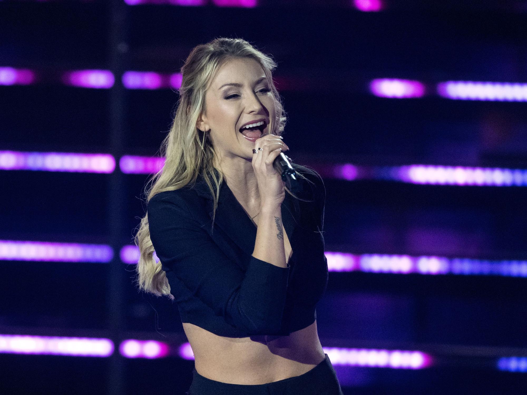 Die deutsche Sängerin Anna-Carina Woitschack steht in der Fernsehshow „Das große Schlagerjubiläum 2022“ in Leipzig auf der Bühne und singt ins Mikrfon. Die Blondine trägt ein schwarzes, bauchfreies Oberteil.
