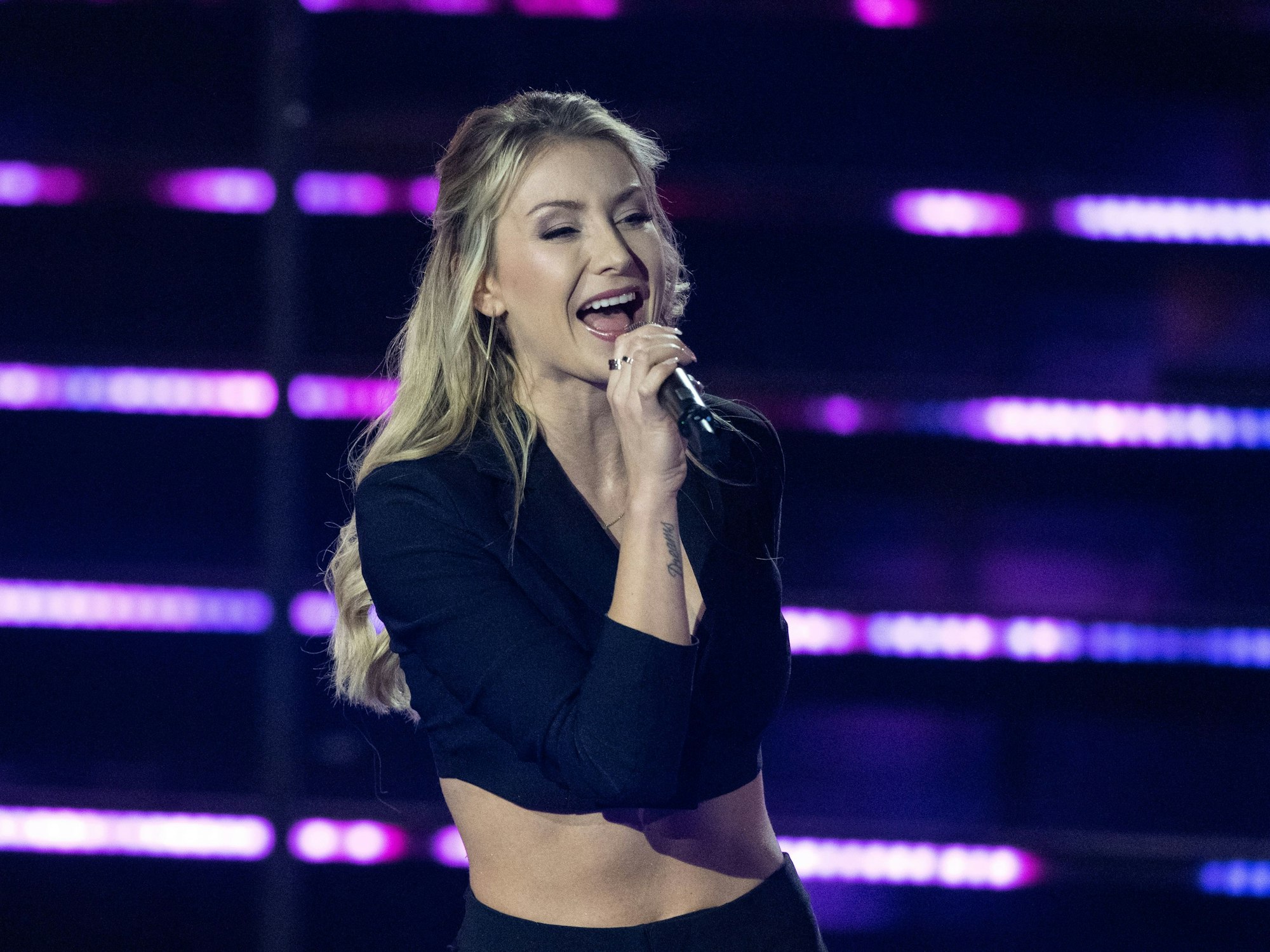 Die deutsche Sängerin Anna-Carina Woitschack steht in der Fernsehshow „Das große Schlagerjubiläum 2022“ in Leipzig auf der Bühne und singt ins Mikrfon. Die Blondine trägt ein schwarzes, bauchfreies Oberteil.