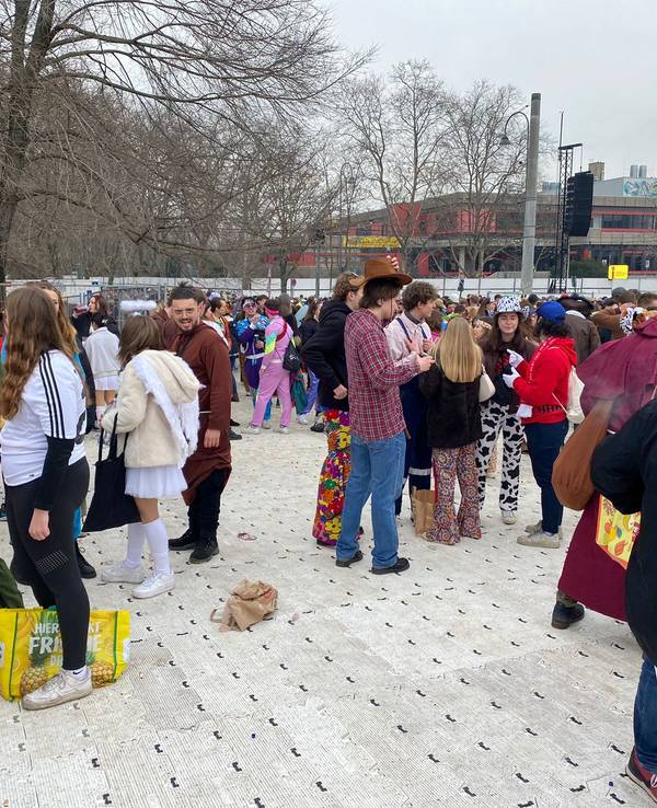 Menschen feiern Karneval auf den abgedeckten Uniwiesen.