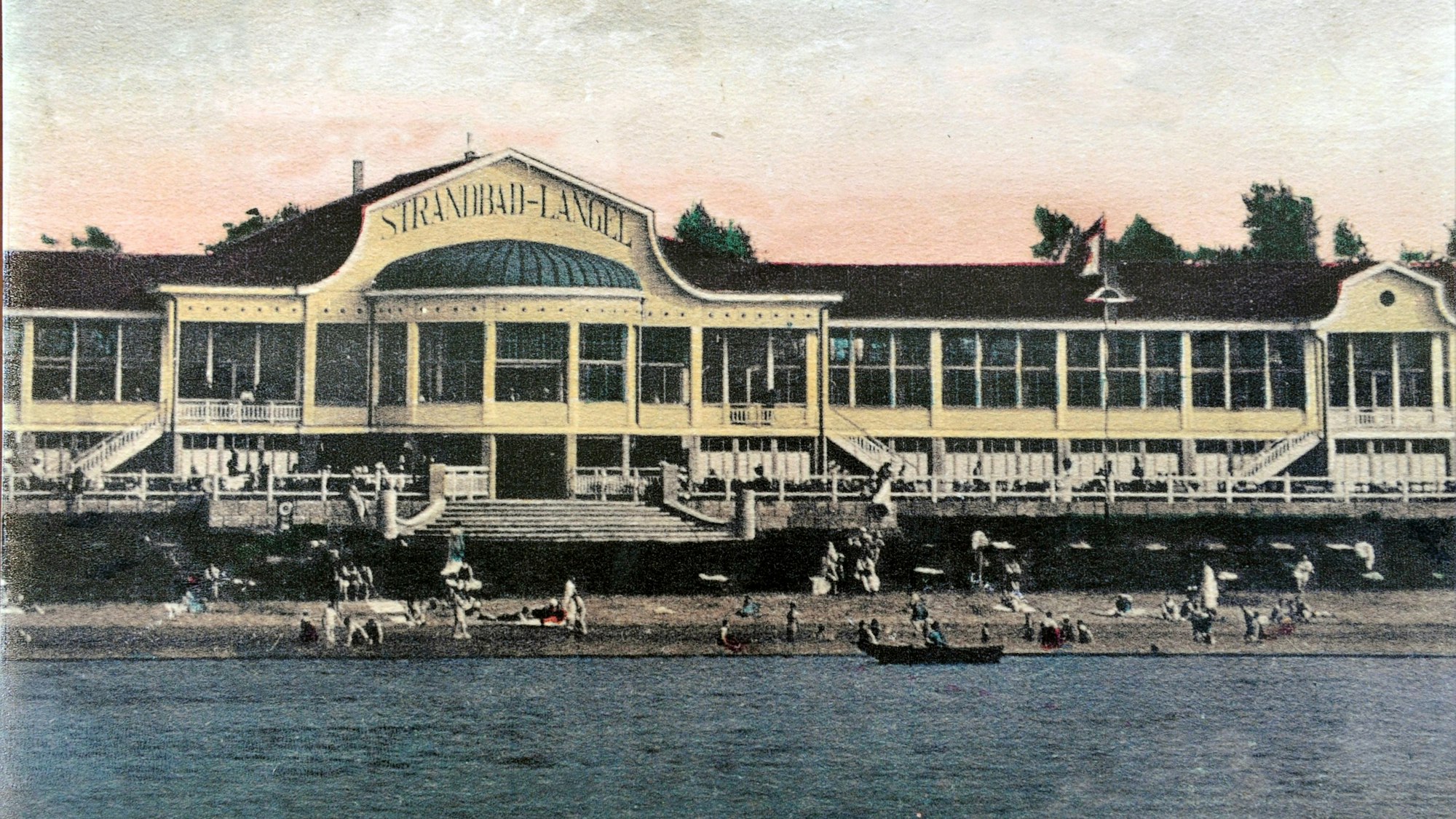 Ein langgestrecktes Gebäude steht am Rheinufer, eine breite Treppe führt hinunter zum Strand, an dem sich mehrere Menschen tummeln.