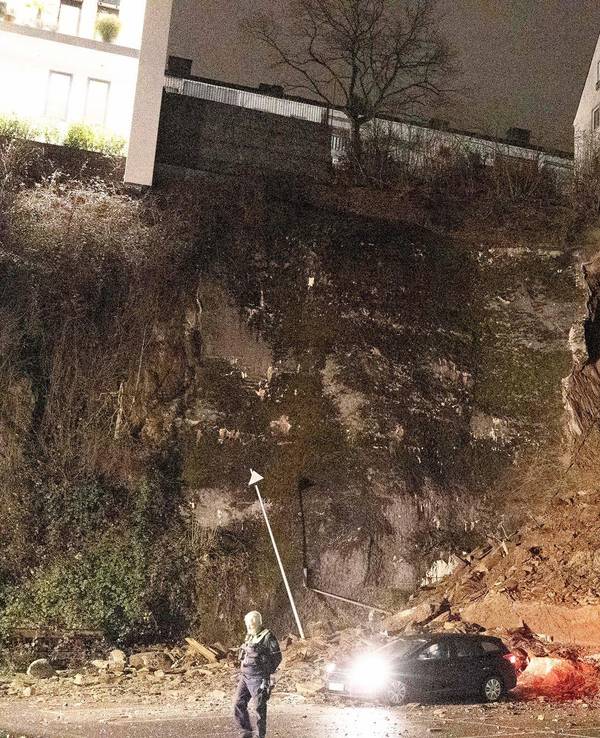 Ein Auto steht noch unterhalb eines abgerutschten Hanges. Wegen des Hangrutsches haben Einsatzkräfte der Polizei und Feuerwehr mehrere Wohnungen am Samstagmorgen (18. Februar 2023) evakuiert.