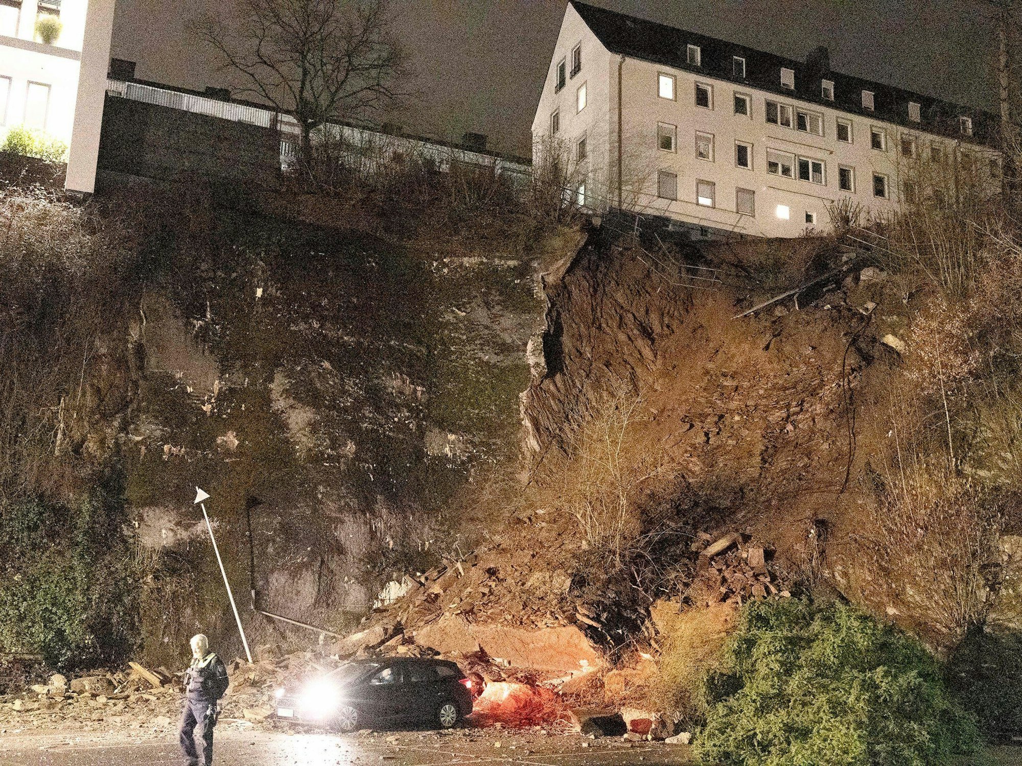 Ein Auto steht noch unterhalb eines abgerutschten Hanges. Wegen des Hangrutsches haben Einsatzkräfte der Polizei und Feuerwehr mehrere Wohnungen am Samstagmorgen (18. Februar 2023) evakuiert.