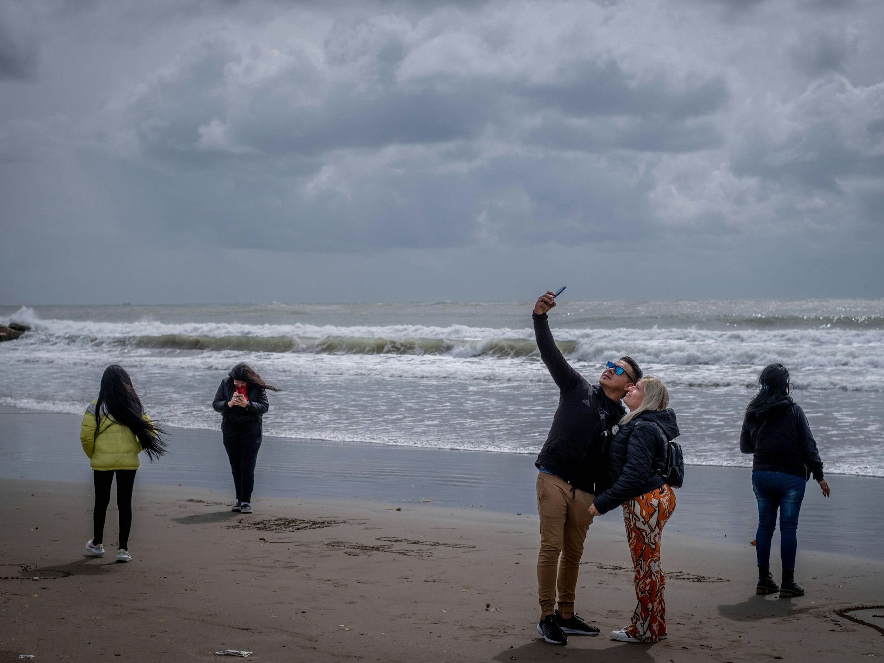 Menschen mit Jacken spazieren am Strand von Mar del Plata (Argentinien) und machen Selfies während des argentinischen Kälteeinbruchs mitten im Sommer.