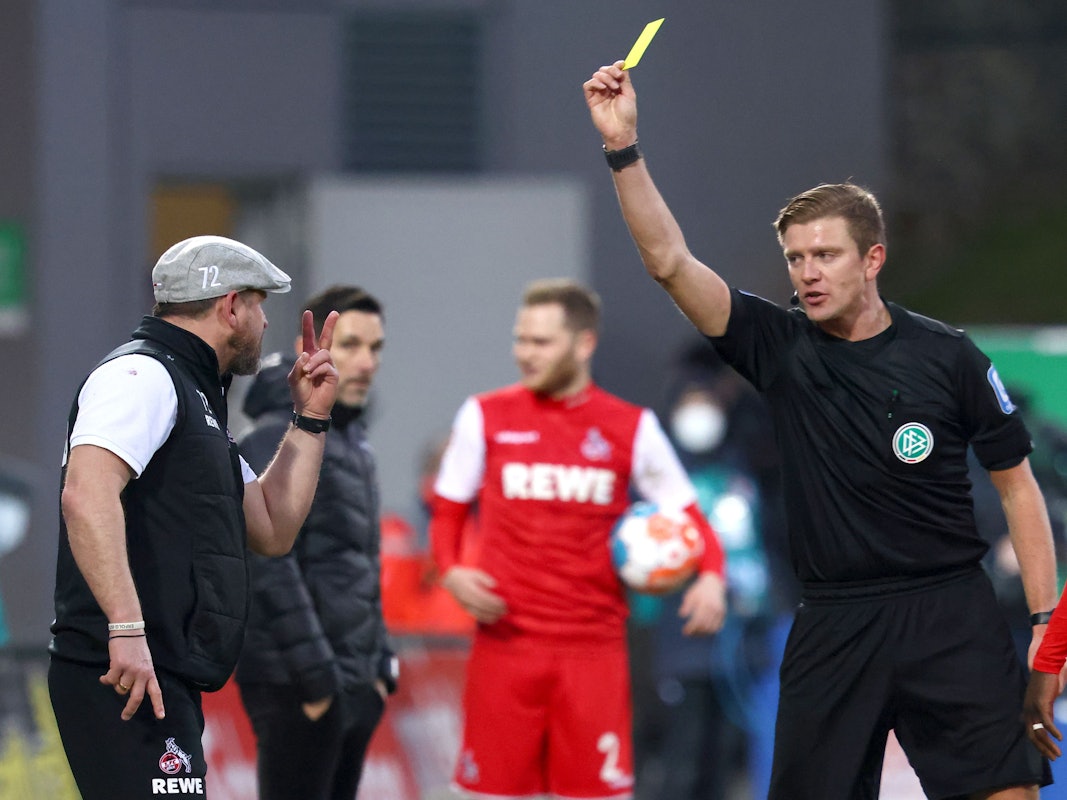 Schiedsrichter Robert Schröder (r) zeigt dem Kölner Trainer Steffen Baumgart (l) die Gelbe Karte.