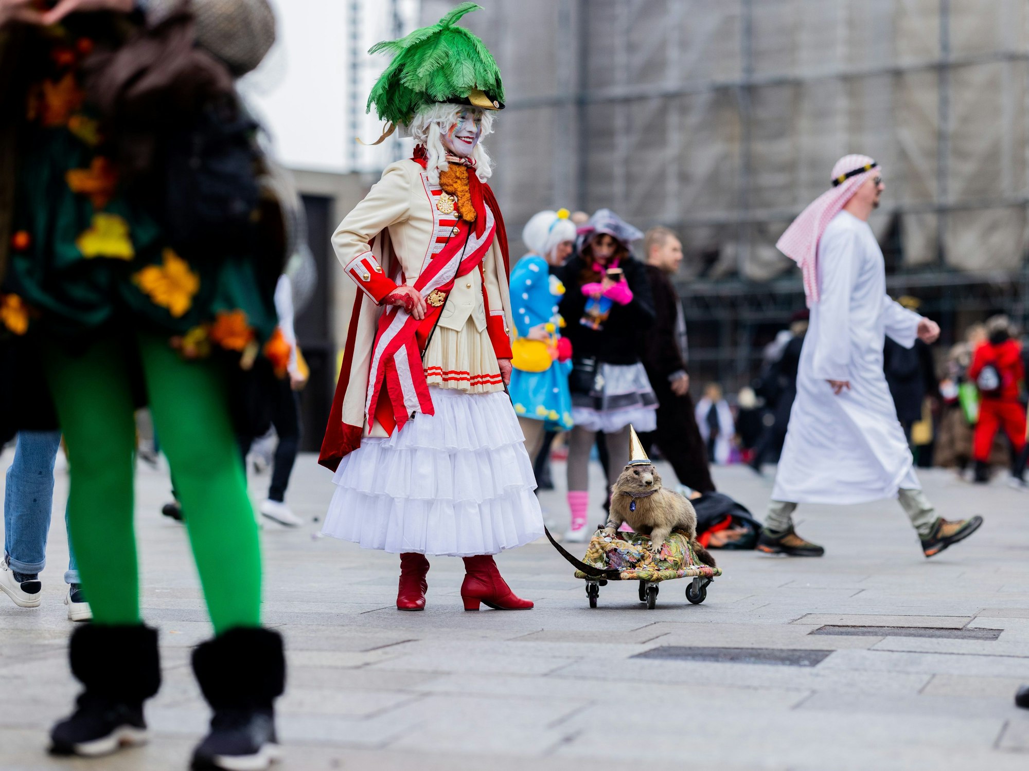 Eine Karnevalistin steht mit einem ausgestopften Murmeltier auf der Domplatte.