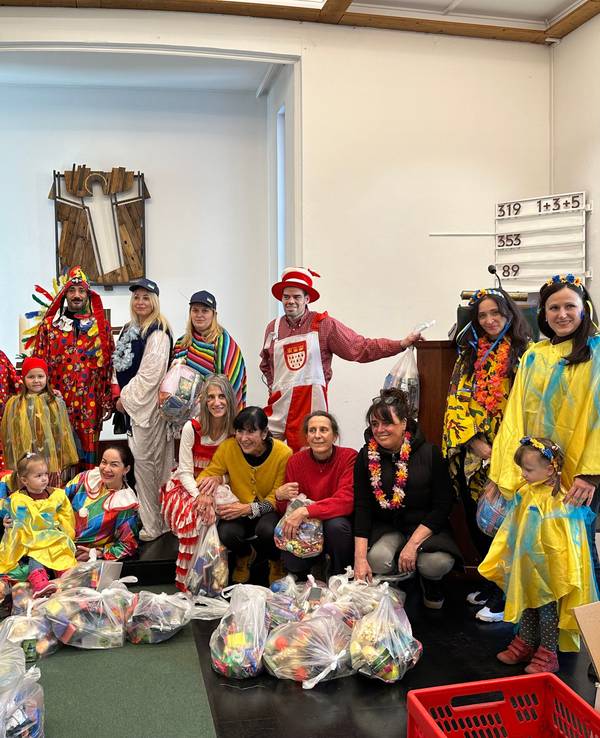 Eine Gruppe von ukrainischen Schutzsuchenden hat zusammen mit Ehrenamtlerinnen und Ehrenamtlern Tüten für den anstehenden Karnevalsumzug in Bergisch Gladbach vorbereitet. Hier posieren alle zusammen für ein Gruppenfoto. Die ukrainischen Schutzsuchenden tragen selbstgebastelte Kostüme in Blau-Gelb.