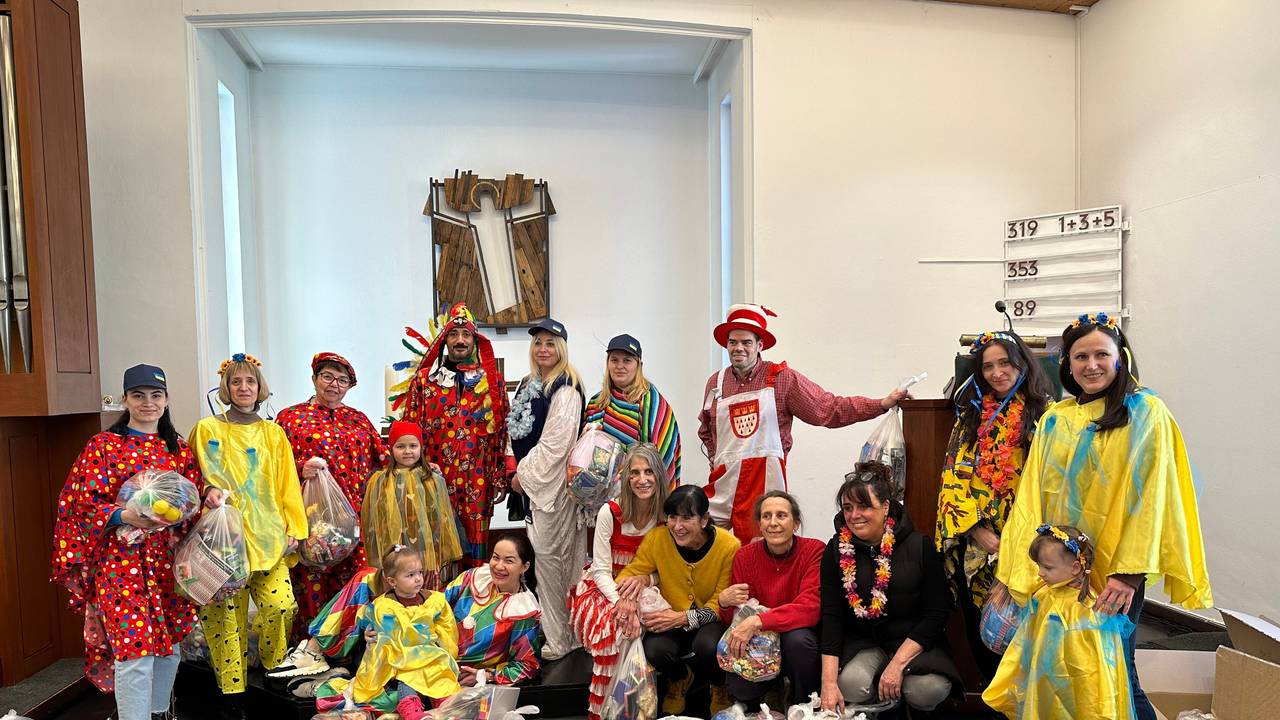 Eine Gruppe von ukrainischen Schutzsuchenden hat zusammen mit Ehrenamtlerinnen und Ehrenamtlern Tüten für den anstehenden Karnevalsumzug in Bergisch Gladbach vorbereitet. Hier posieren alle zusammen für ein Gruppenfoto. Die ukrainischen Schutzsuchenden tragen selbstgebastelte Kostüme in Blau-Gelb.