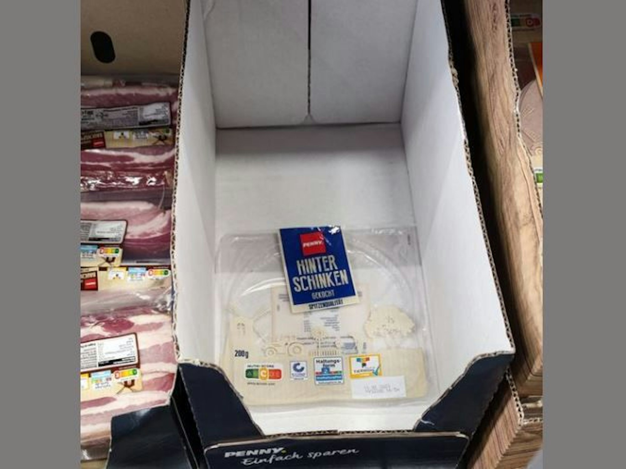 Ein leerer Karton mit einer leeren Schinken-Verpackung steht in einem Regal des Discounters Penny.