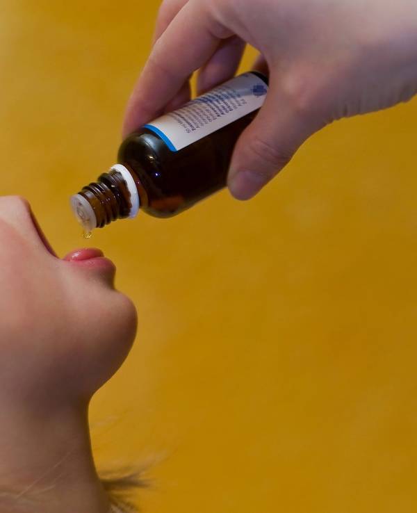 Das Symbolfoto von 2009 zeigt ein Kleinkind mit geöffnetem Mund. Es bekommt flüssige Medizin aus einer braunen Glasflasche auf die Zunge geträufelt.