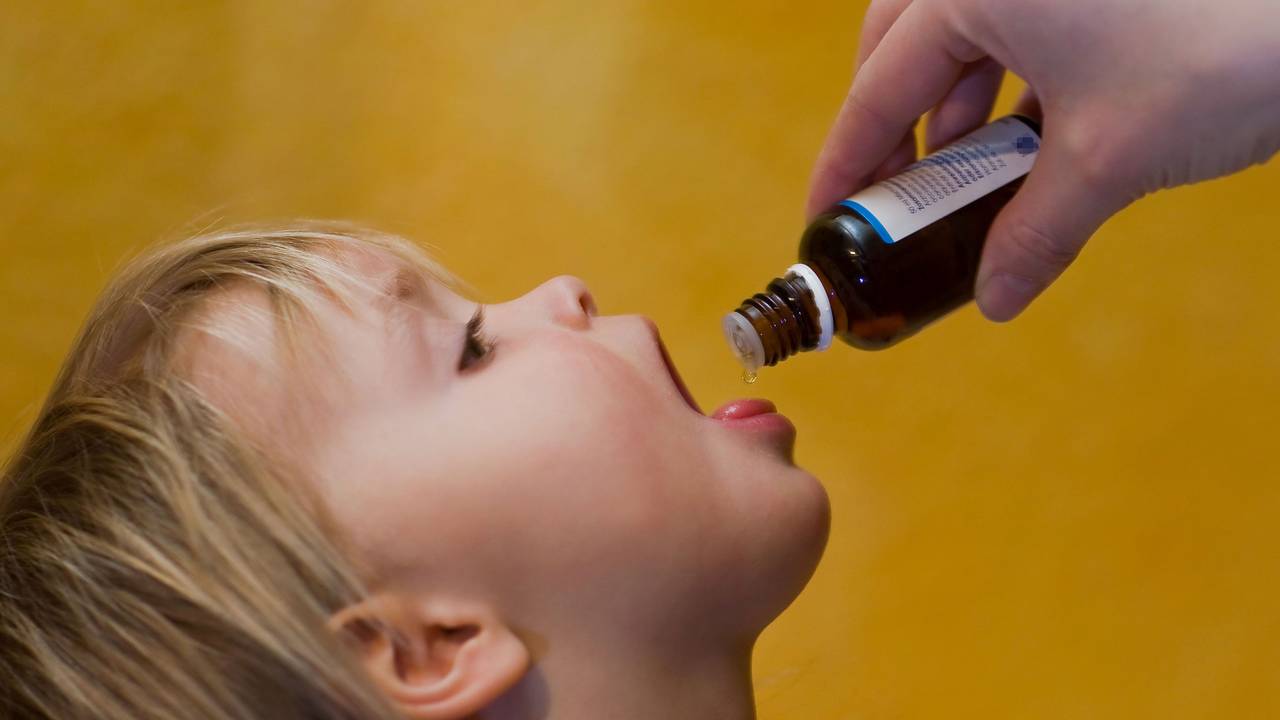 Das Symbolfoto von 2009 zeigt ein Kleinkind mit geöffnetem Mund. Es bekommt flüssige Medizin aus einer braunen Glasflasche auf die Zunge geträufelt.