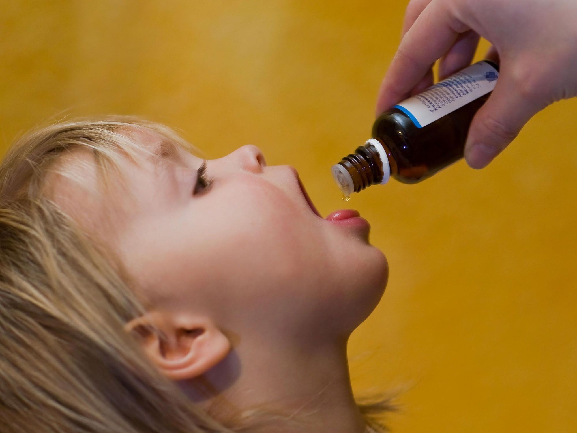 Das Symbolfoto von 2009 zeigt ein Kleinkind mit geöffnetem Mund. Es bekommt flüssige Medizin aus einer braunen Glasflasche auf die Zunge geträufelt.