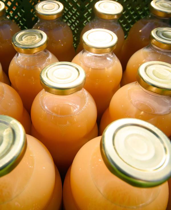 Das Symbolfoto von 2021 zeigt mehrere Glasflaschen mit Deckel. In den Flaschen befindet sich ein orangefarbener Saft.