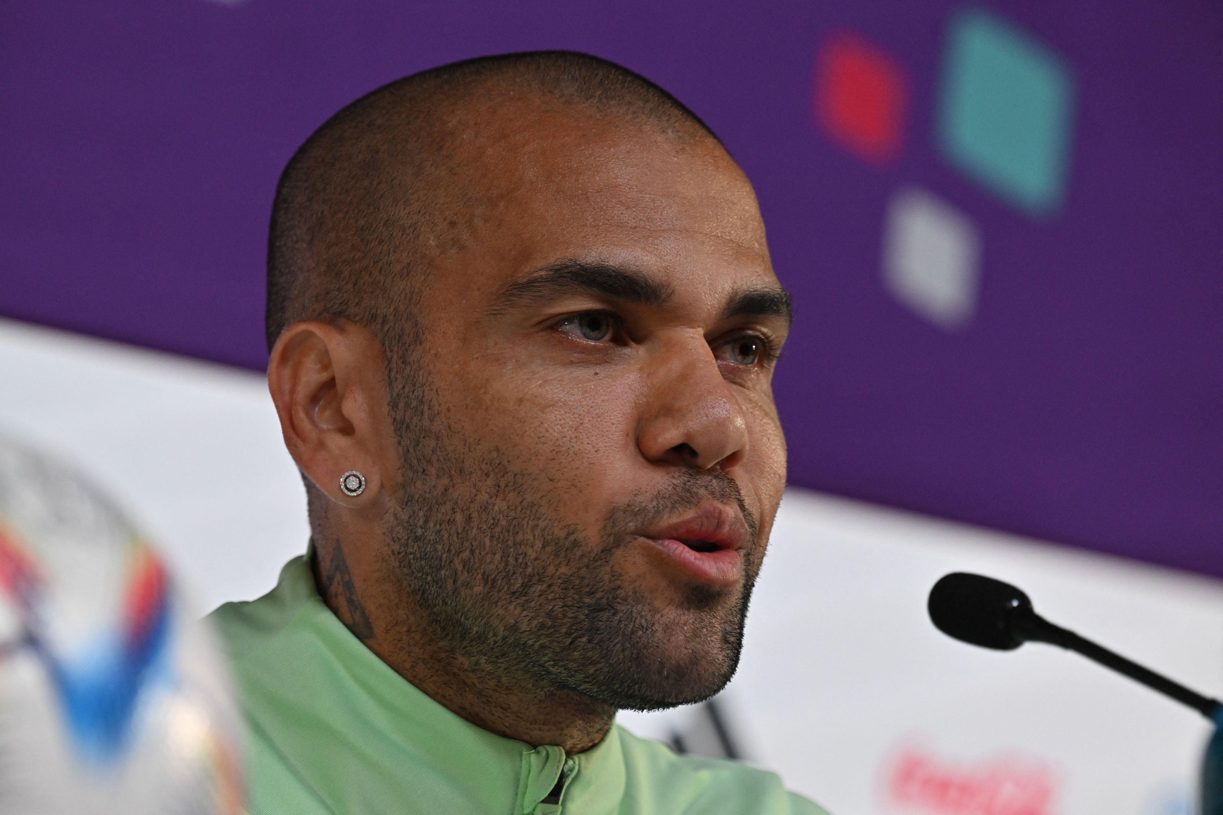 Dani Alves sitzt bei einer Pressekonferenz am Rednerpult.