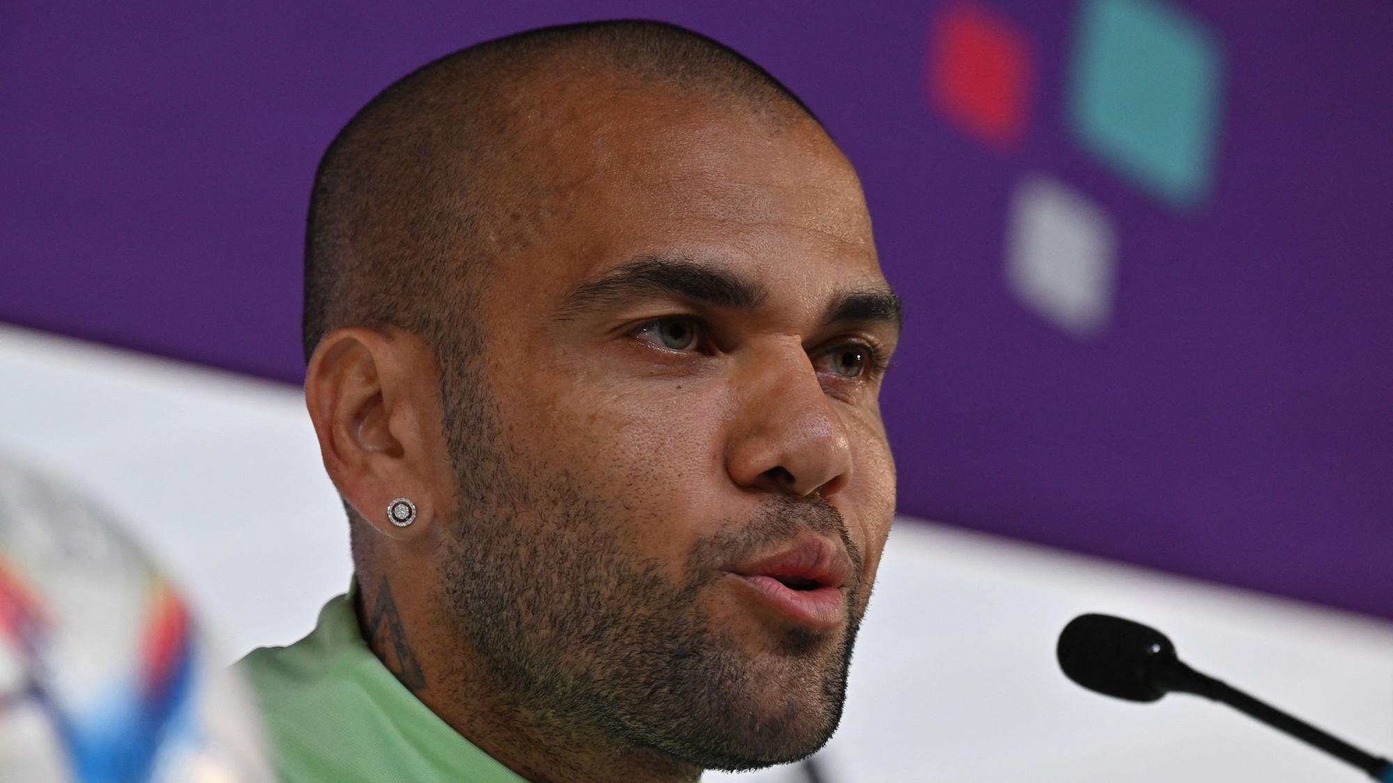 Dani Alves sitzt bei einer Pressekonferenz am Rednerpult.