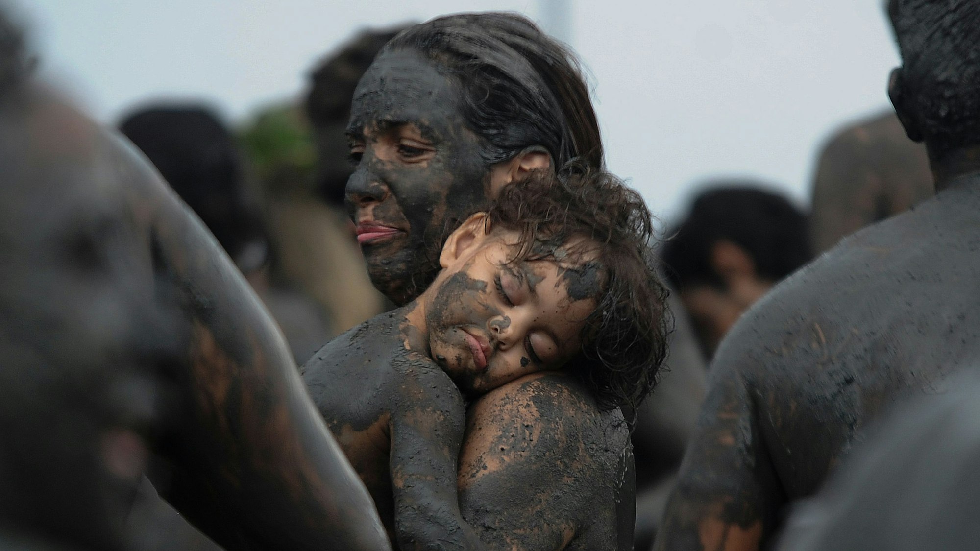 Ein kleiner, mit Schlamm beschmierter Junge schläft auf dem Arm seiner Mutter.